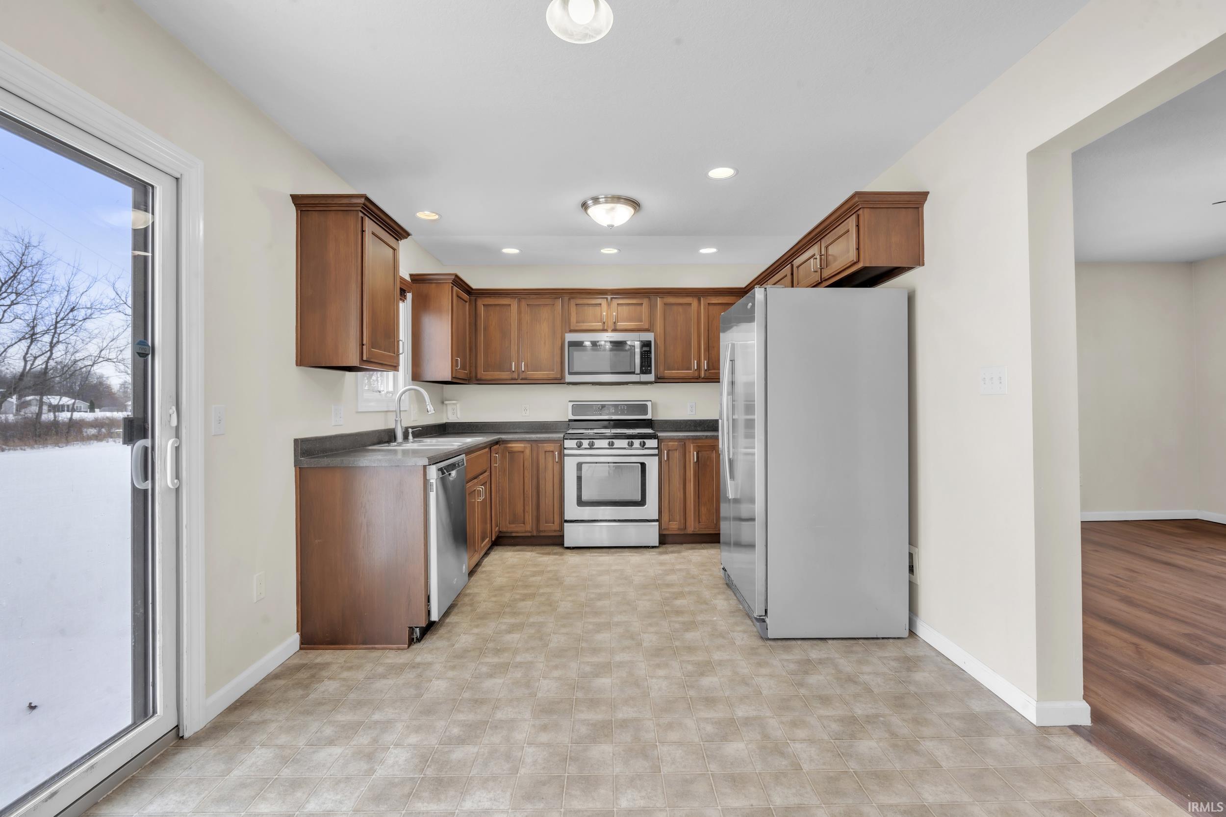 Kitchen with appliances with stainless steel finishes, dark countertops, brown cabinetry, recessed lighting, and light flooring