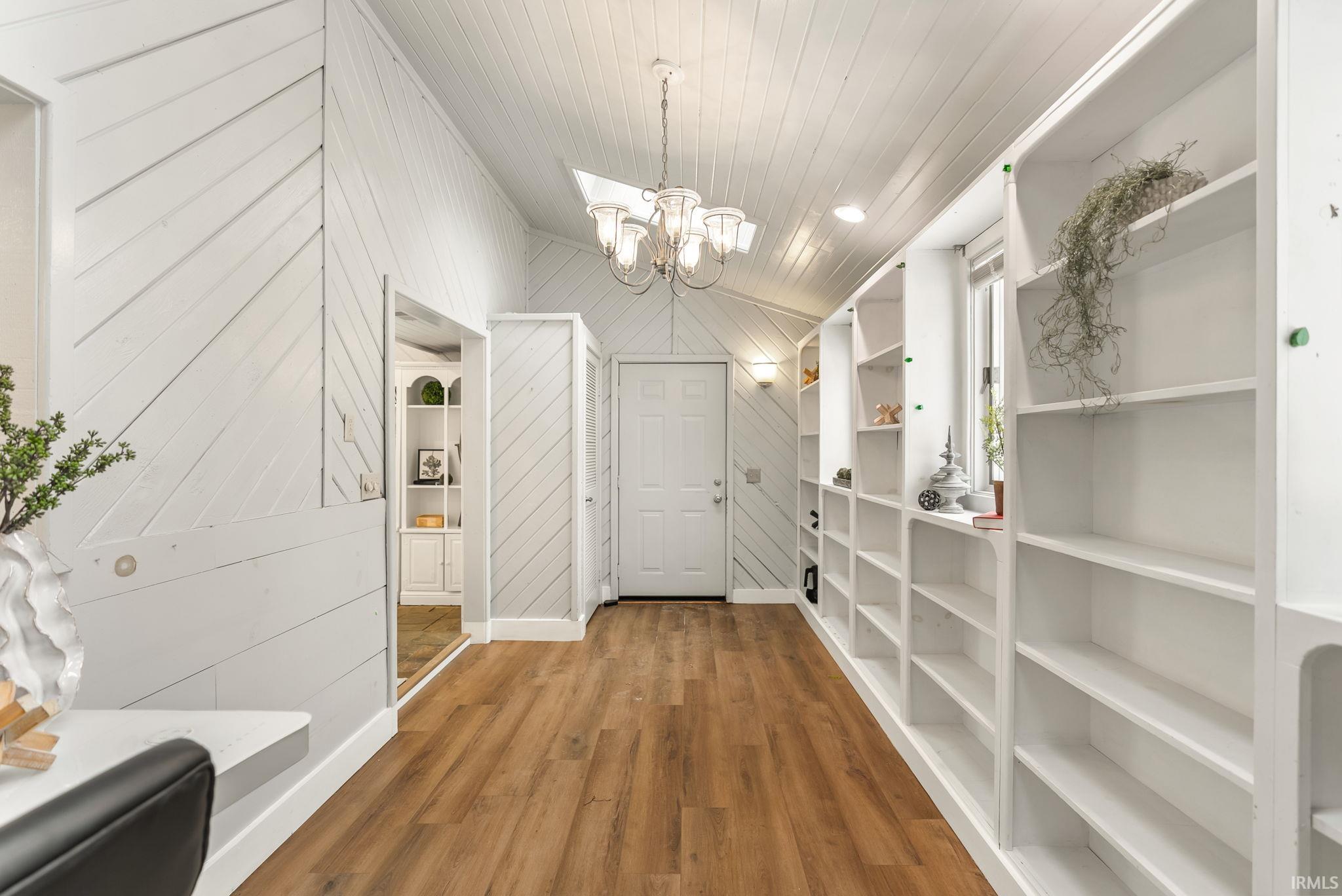 Hallway featuring built in features, wood walls, a chandelier, wood finished floors, and wooden ceiling
