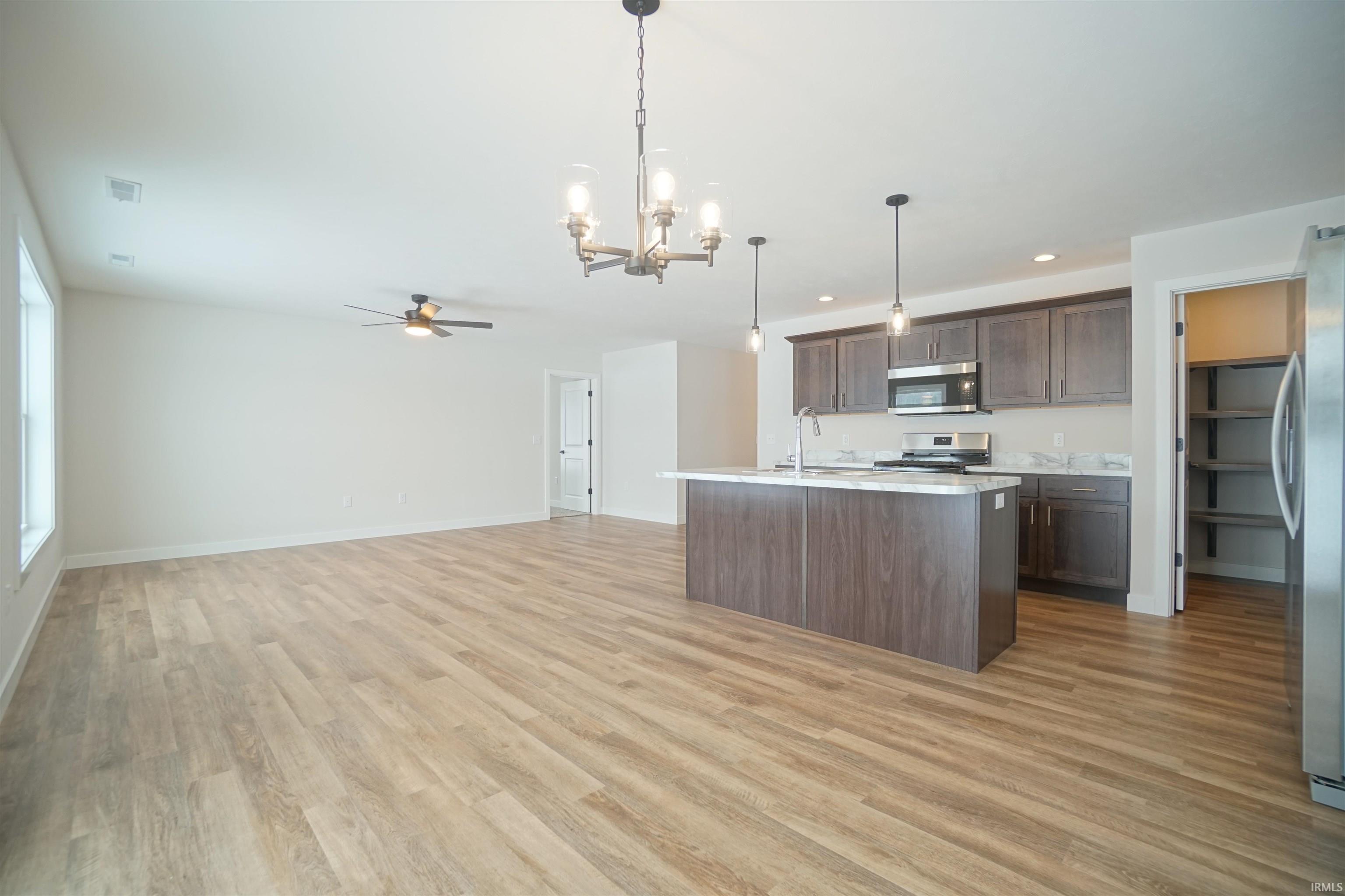 Kitchen with a chandelier, decorative light fixtures, dark brown cabinetry, ceiling fan, and an island with sink