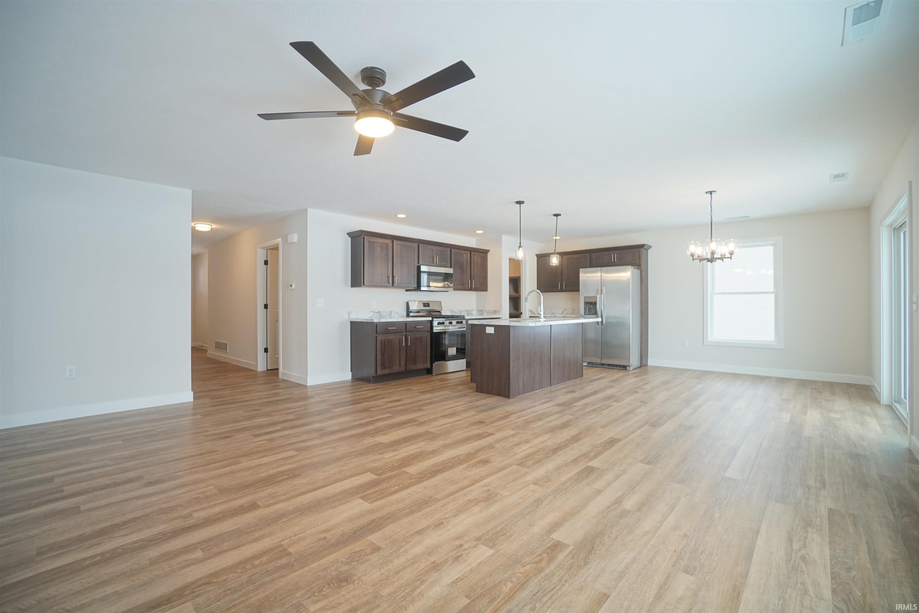 Kitchen with open floor plan, light countertops, dark brown cabinets, pendant lighting, and stainless steel appliances