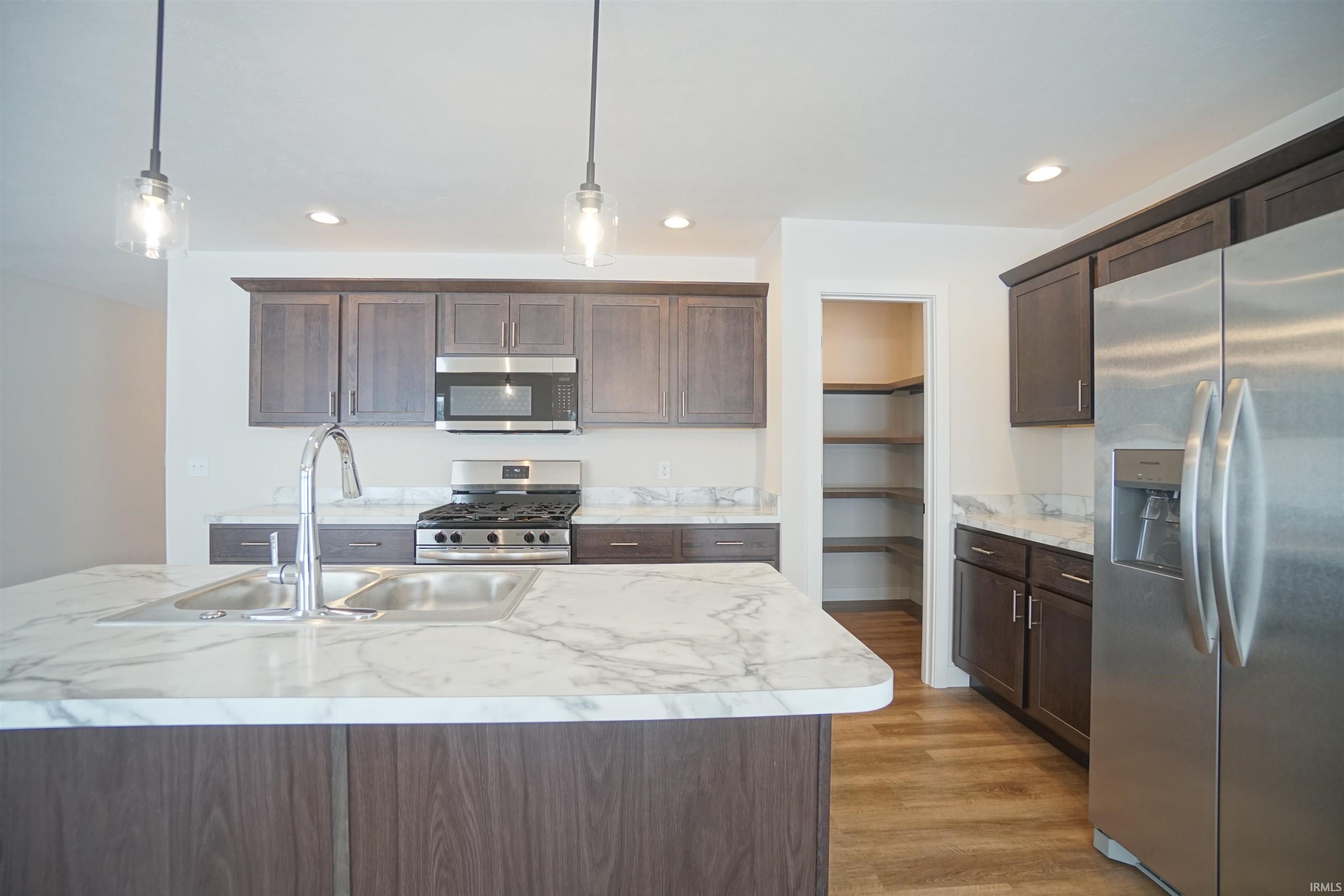 Kitchen featuring appliances with stainless steel finishes, dark brown cabinets, hanging light fixtures, recessed lighting, and light wood finished floors