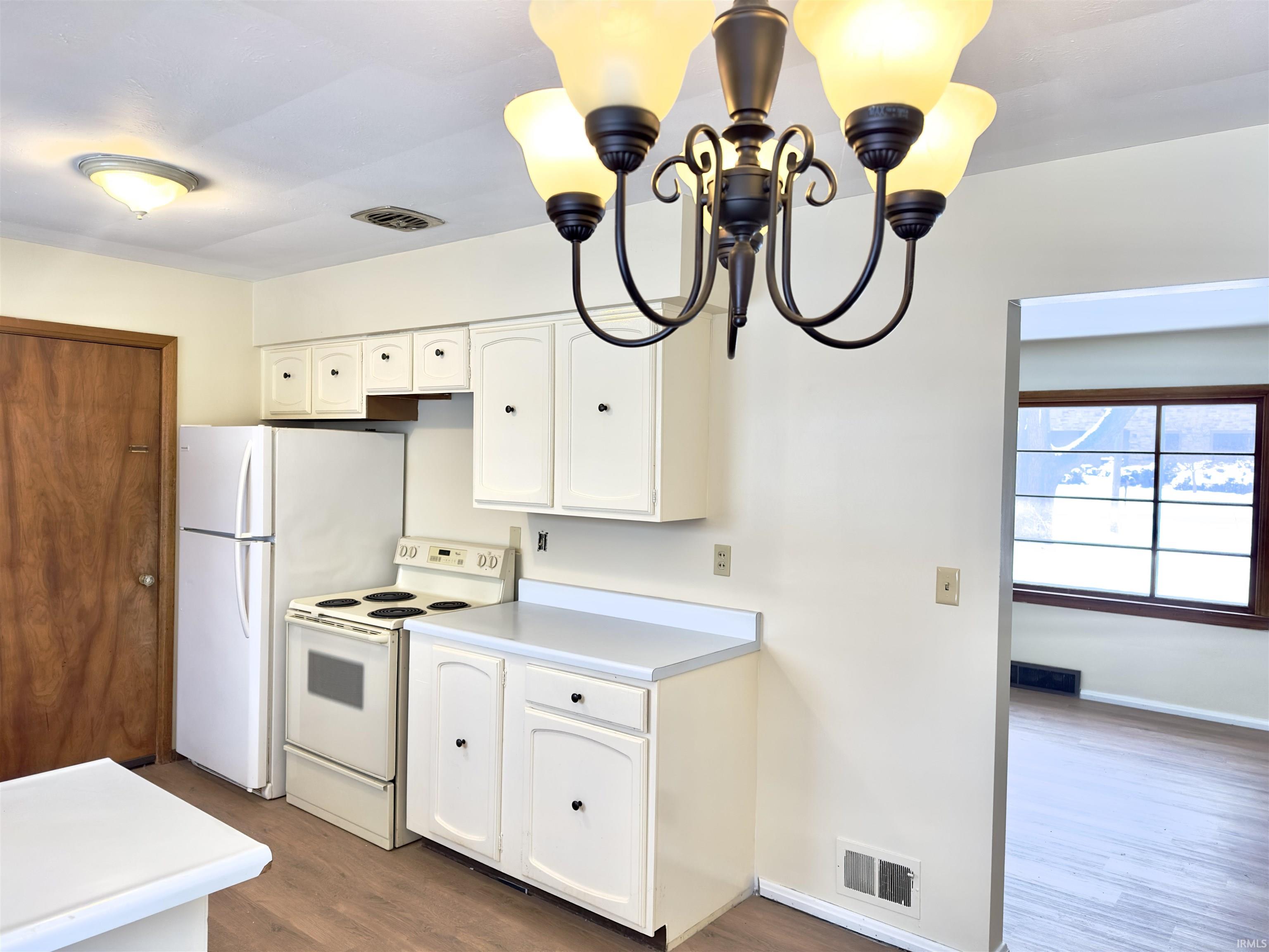 Kitchen featuring white appliances, light countertops, a chandelier, dark wood-style floors, and white cabinetry