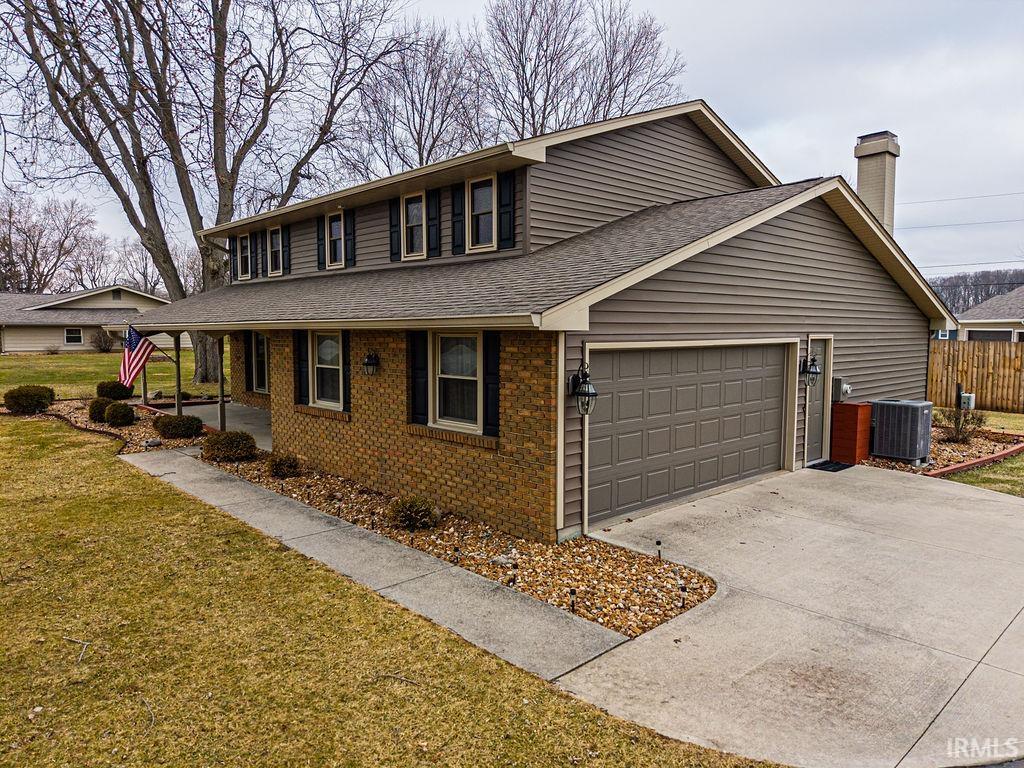 View of front of property featuring driveway, an attached garage, a shingled roof, a chimney, and brick siding