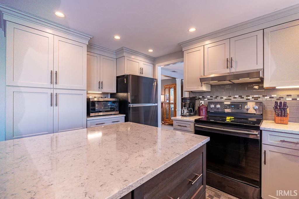 Kitchen with appliances with stainless steel finishes, light stone counters, under cabinet range hood, backsplash, and recessed lighting