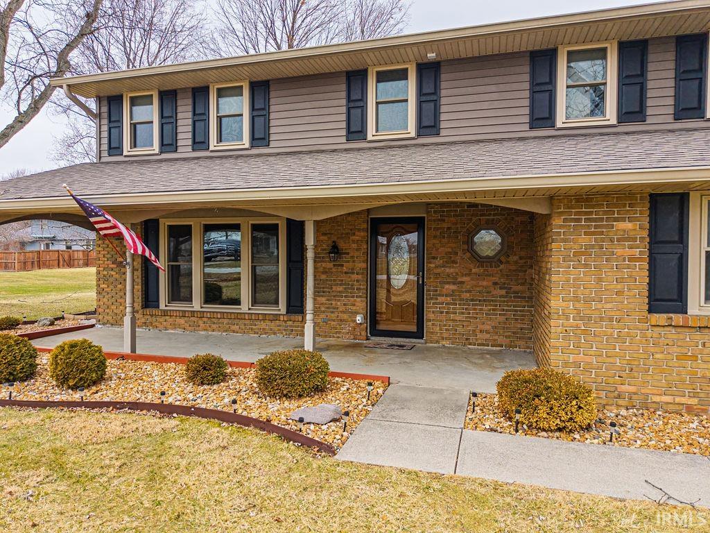 View of front facade featuring covered porch, a front lawn, and brick siding