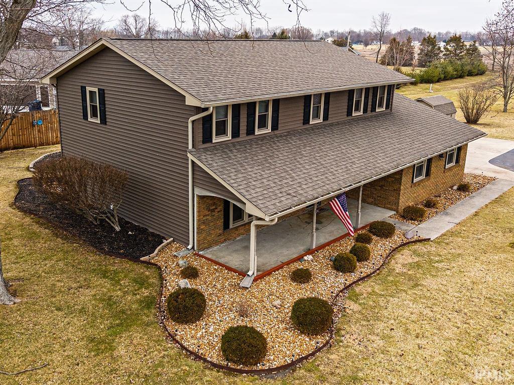 Rear view of property with a shingled roof, a patio, and a lawn