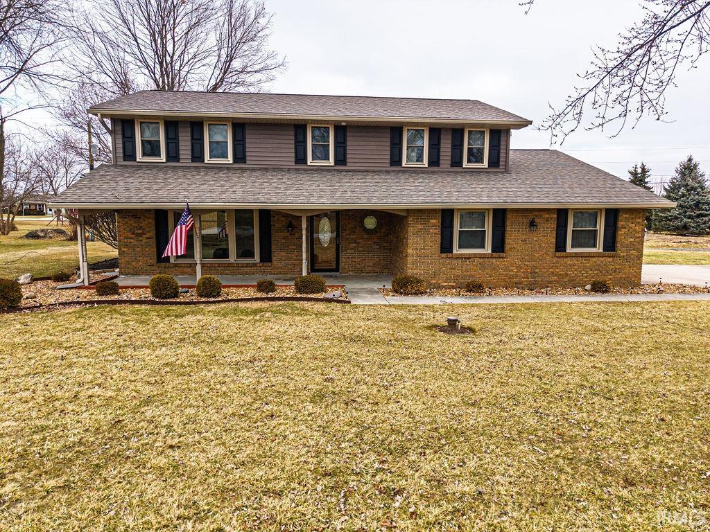 View of front of home featuring a porch, a front yard, a shingled roof, and brick siding