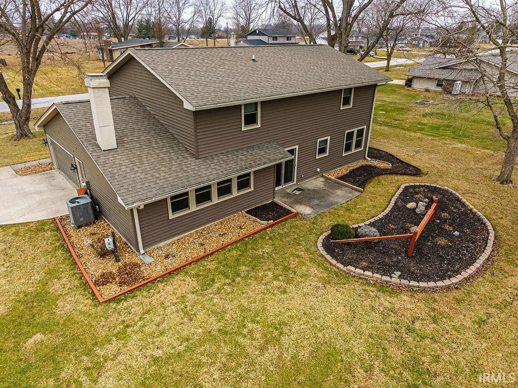 Back of house featuring roof with shingles, a patio, a lawn, and concrete driveway