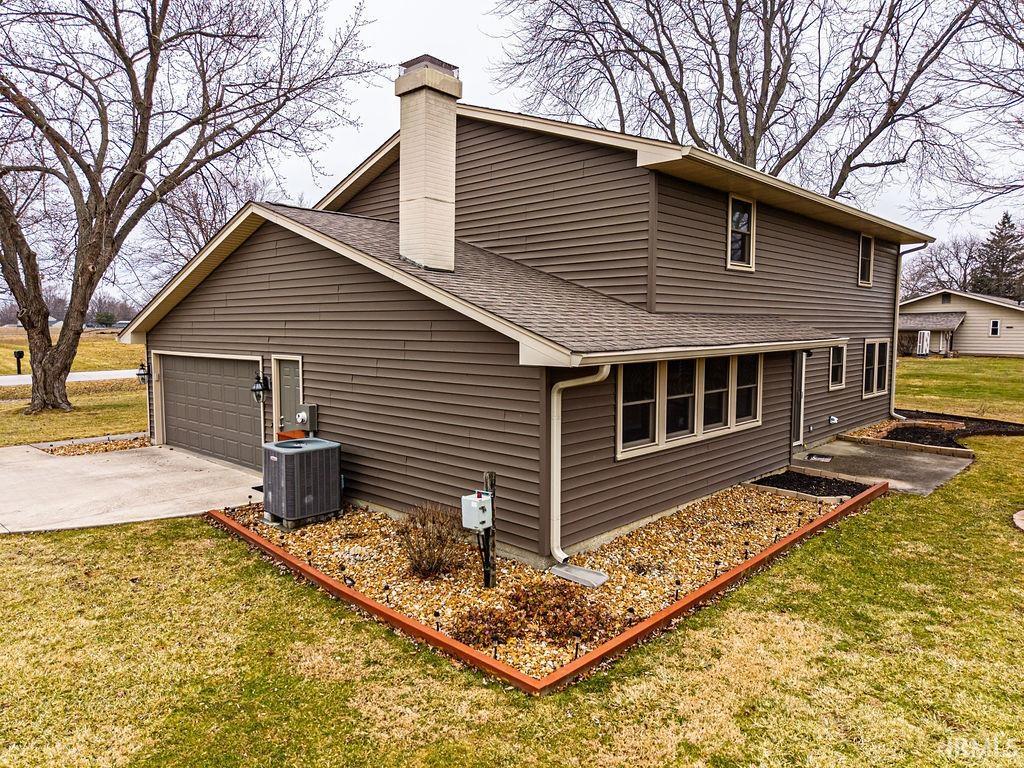 View of home's exterior featuring a lawn, a chimney, roof with shingles, concrete driveway, and a patio