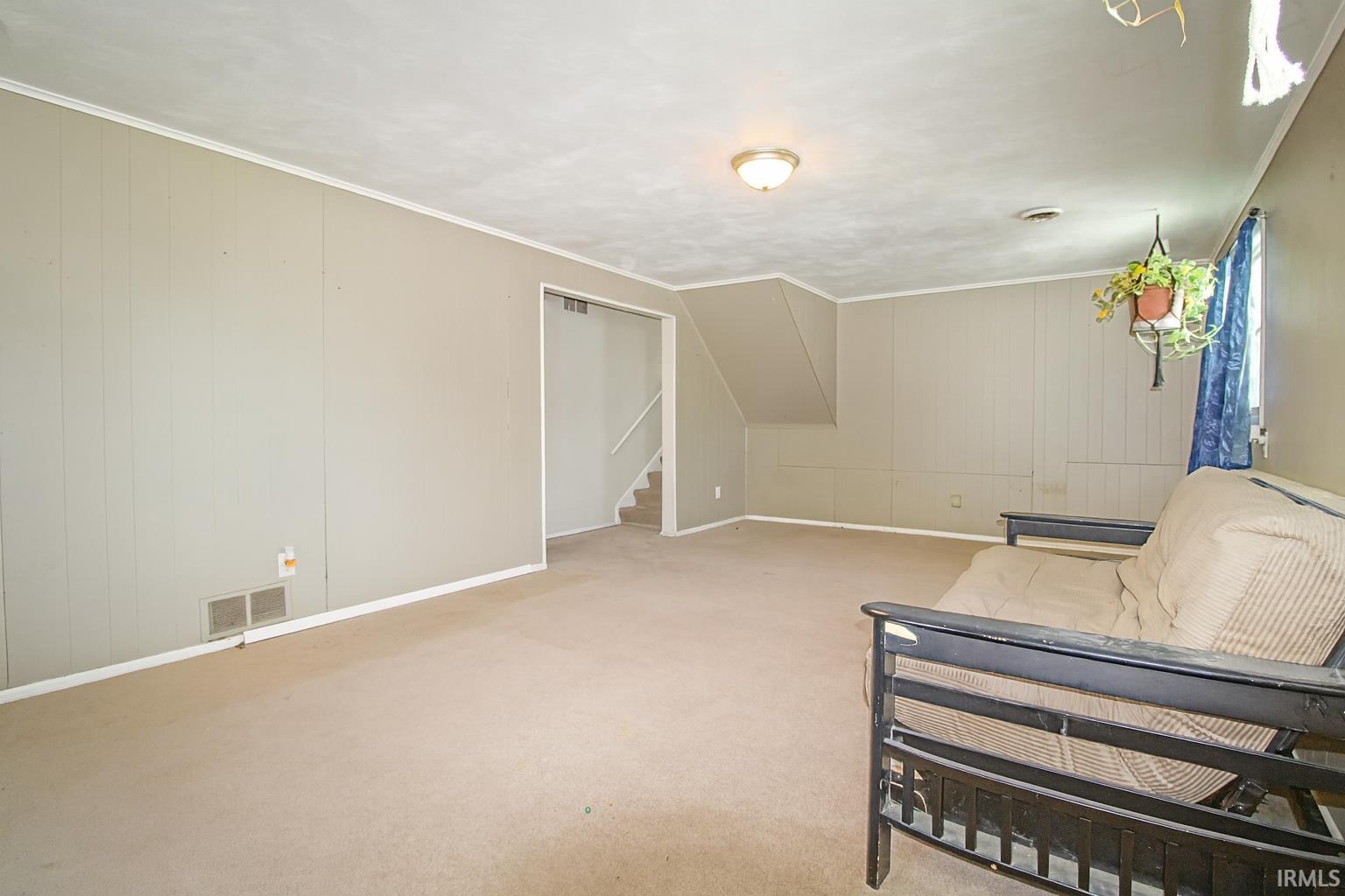 Unfurnished room featuring stairway, ornamental molding, wood walls, carpet flooring, and a decorative wall