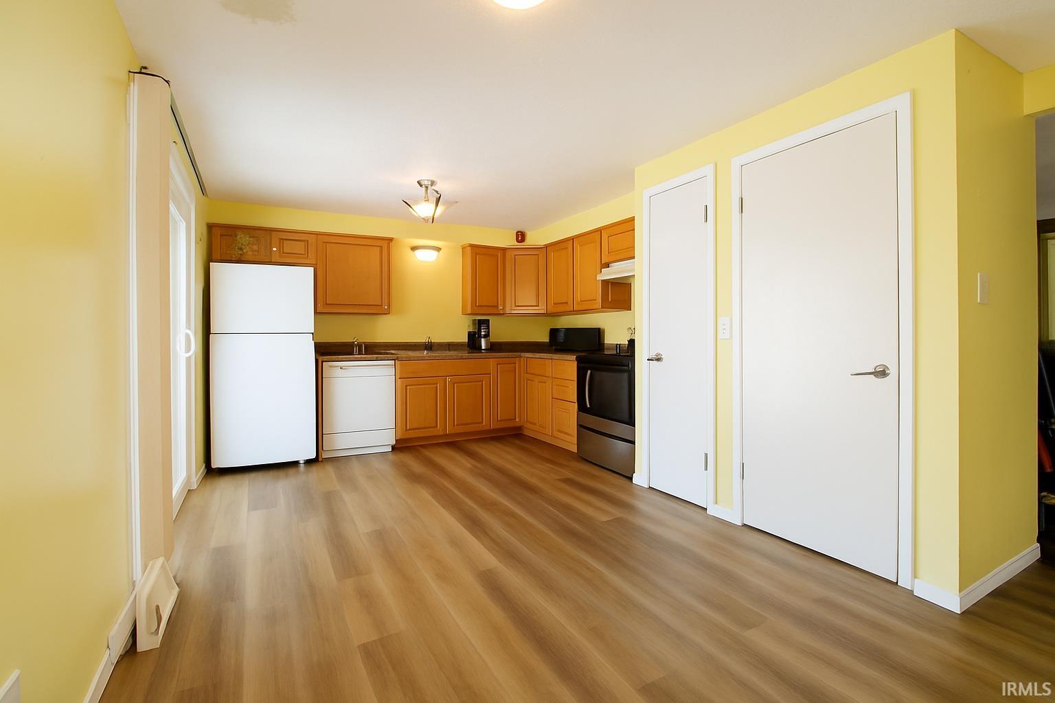 Kitchen featuring white appliances, light wood finished floors, dark countertops, and under cabinet range hood