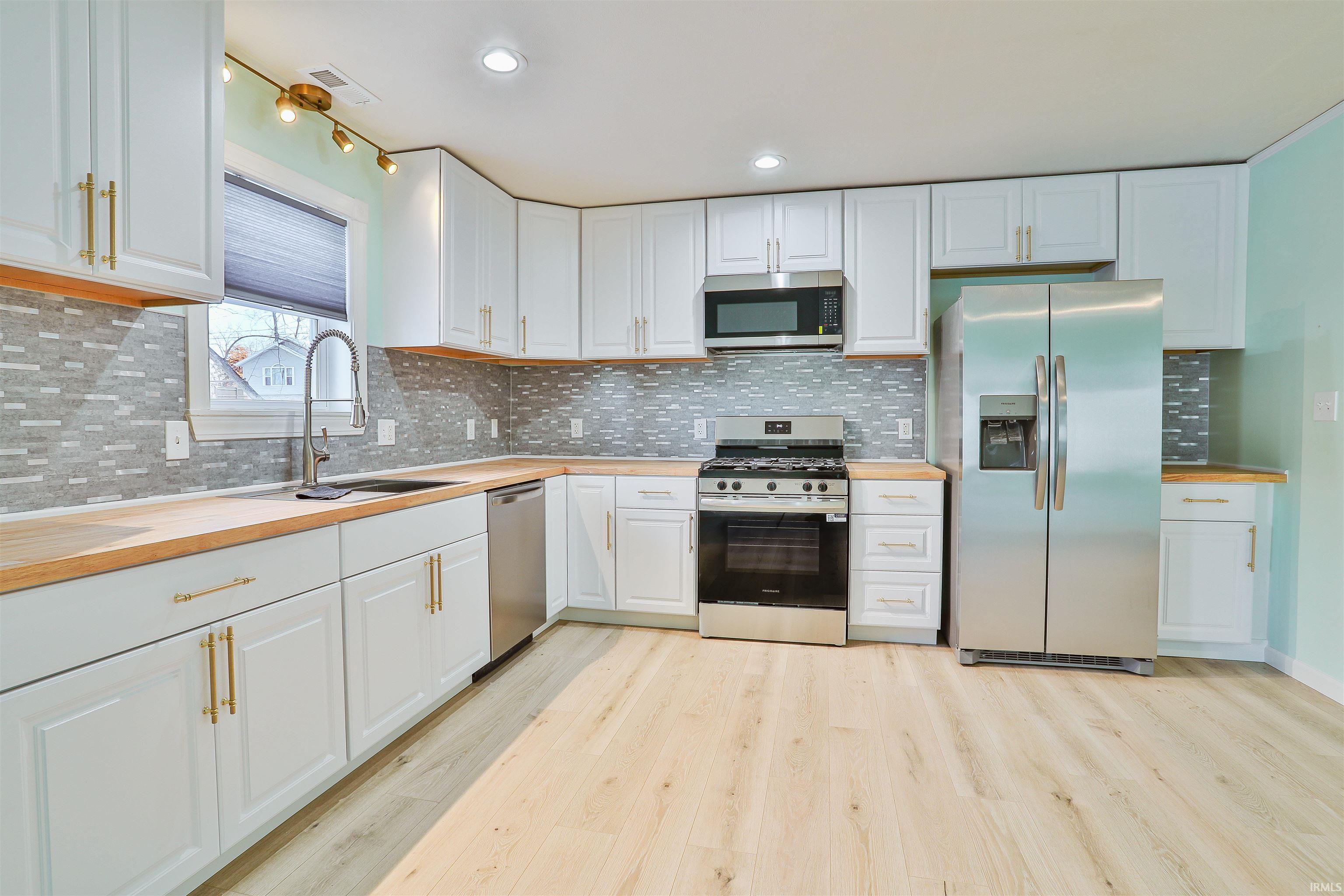 Kitchen featuring appliances with stainless steel finishes, decorative backsplash, white cabinets, light wood-style flooring, and recessed lighting