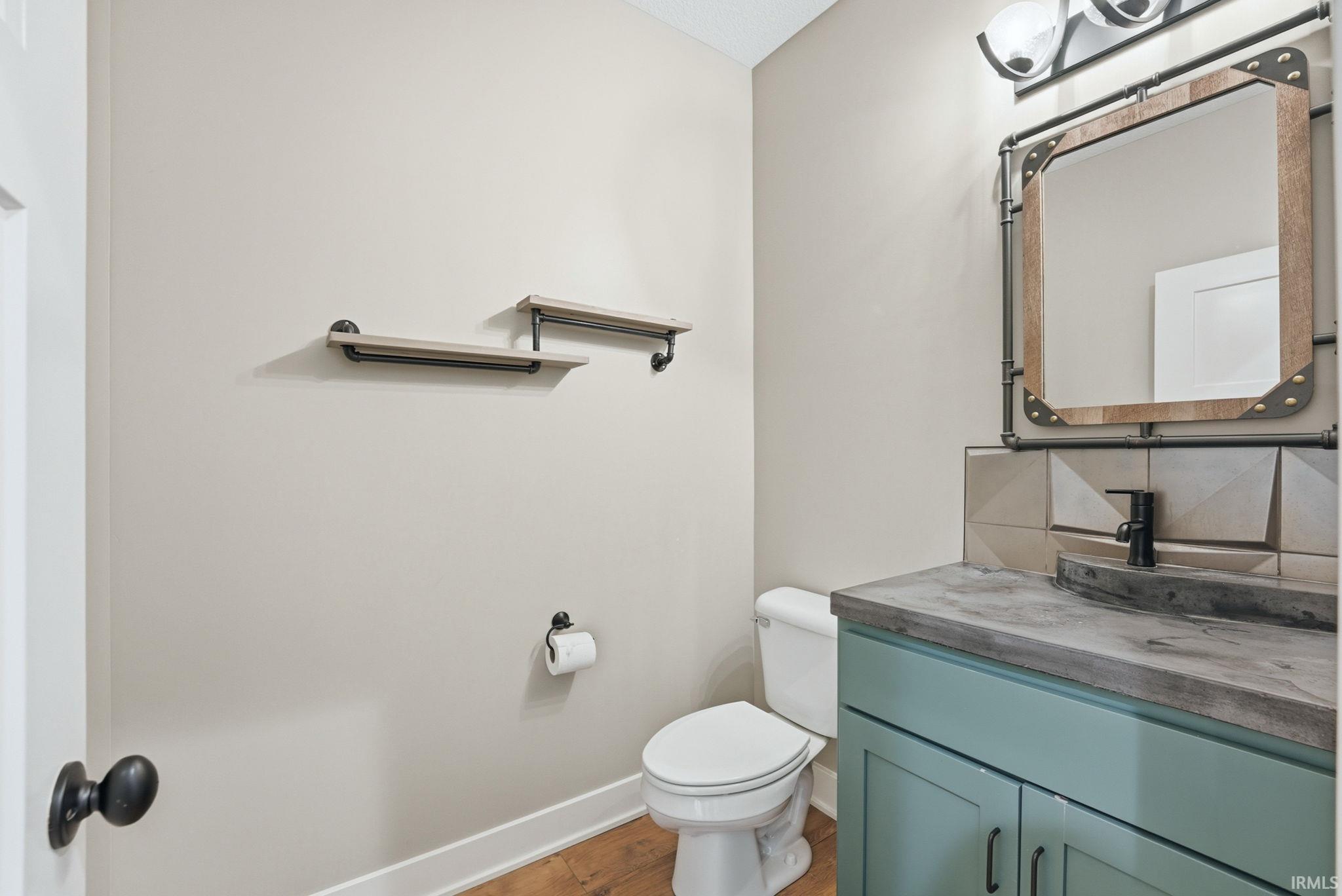 Powder room featuring a sage green vanity with a gray concrete countertop, an industrial-style mirror, a black faucet