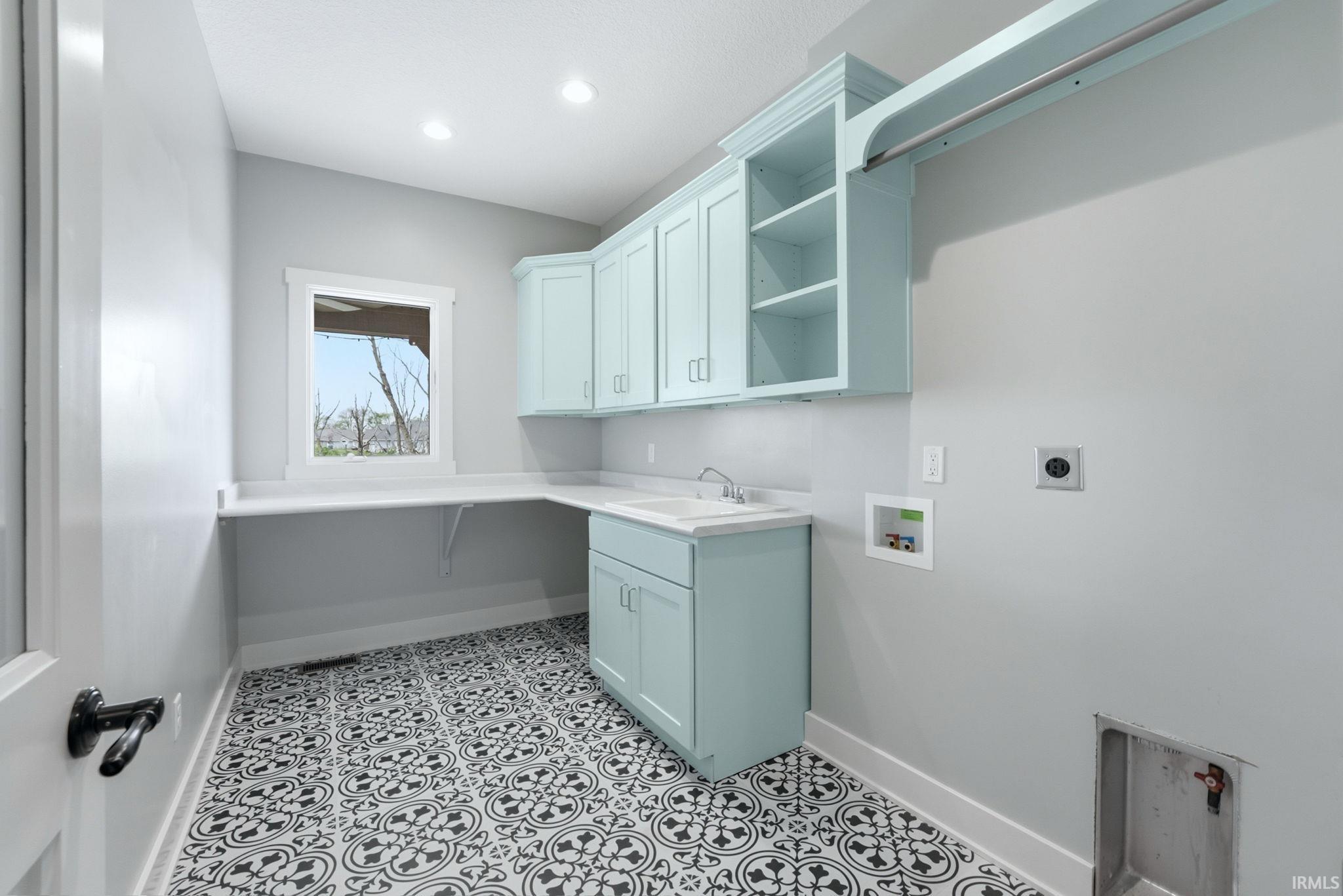 Utility room featuring patterned floor, light blue cabinetry with brushed nickel hardware, integrated sink, and an extended countertop workspace
