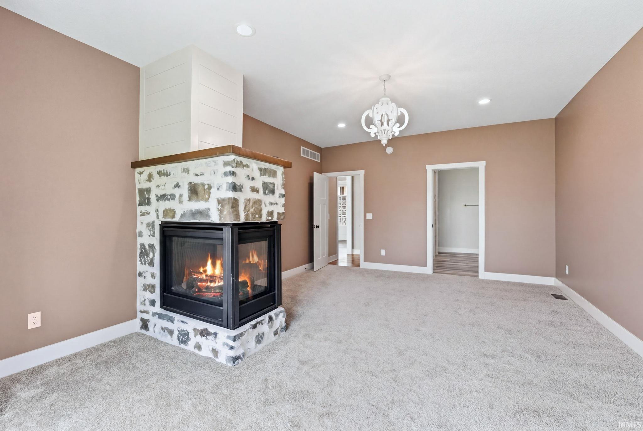 Expansive interior space featuring a corner stone fireplace with a wood mantle, a decorative chandelier, recessed lighting, and soft carpet flooring