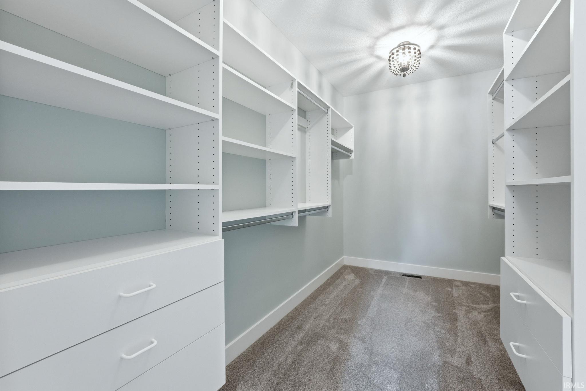 Walk-in closet featuring built-in white shelving, integrated drawers, hanging rods, recessed lighting, and grey carpeting