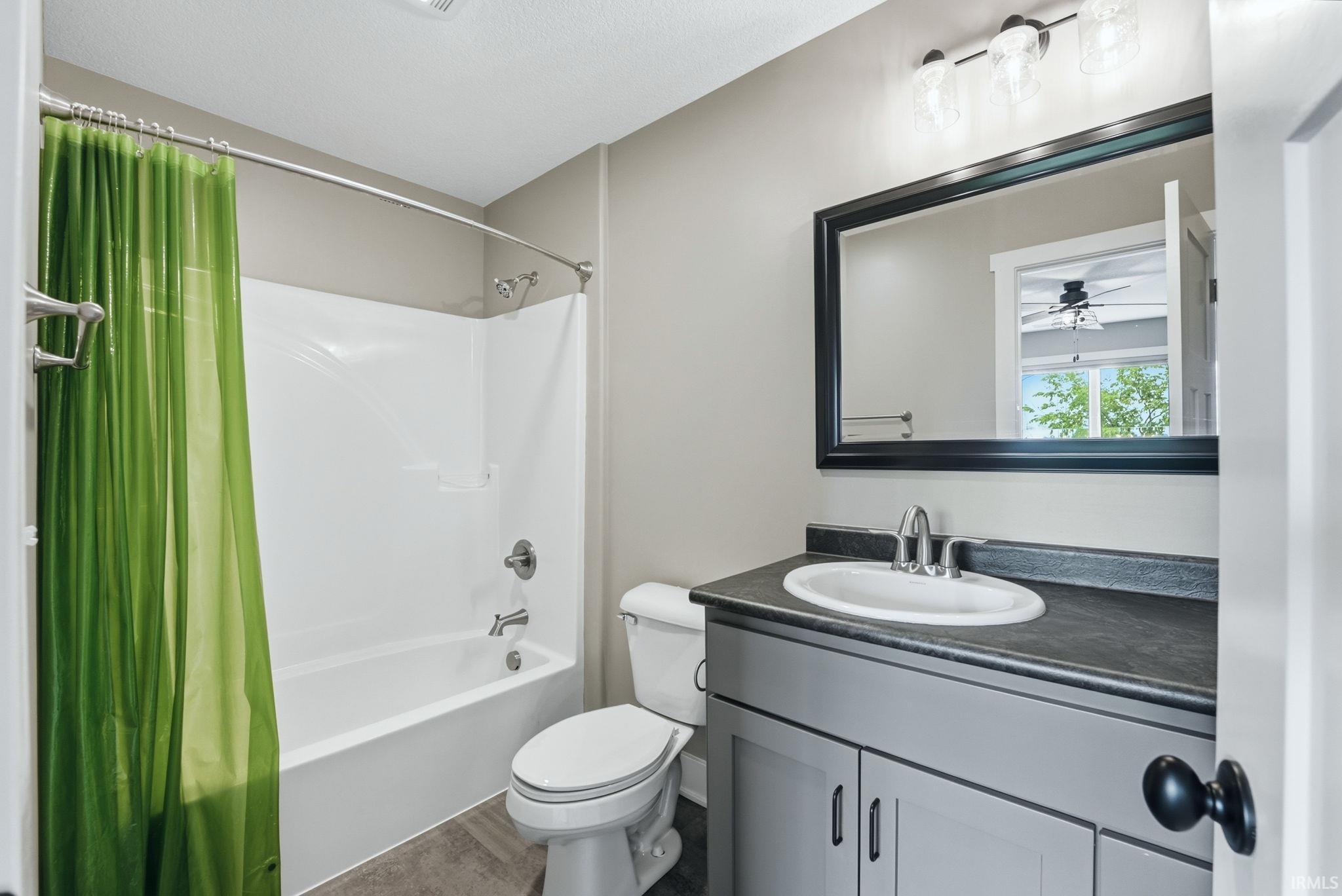 Contemporary bathroom featuring a white bathtub/shower combination, a vanity with a white basin and dark countertop, a framed mirror, and a wall-mounted light fixture