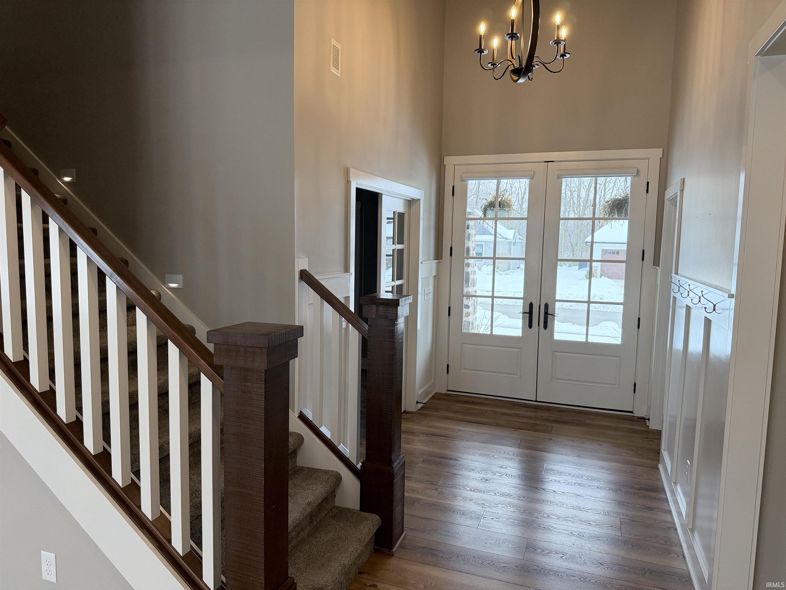 Foyer with a high ceiling, french doors, hardwood / wood-style floors, a chandelier, and stairs