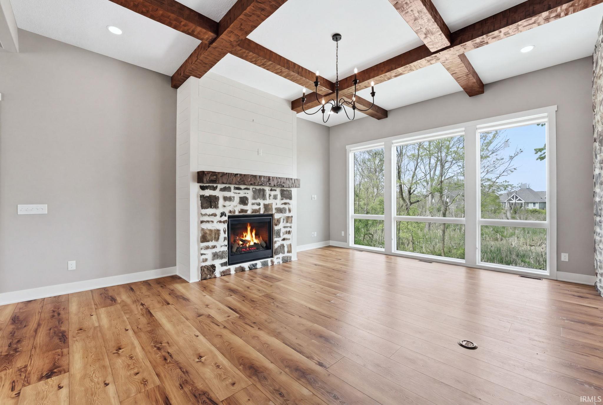 Expansive living space featuring a stone fireplace with a shiplap accent wall, a coffered ceiling with exposed wood beams, and a black chandelier