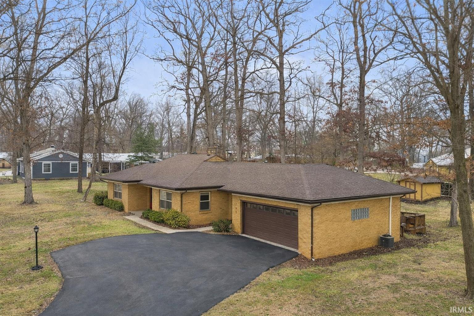 View of front of house with a shingled roof, driveway, brick siding, a front lawn, and a garage