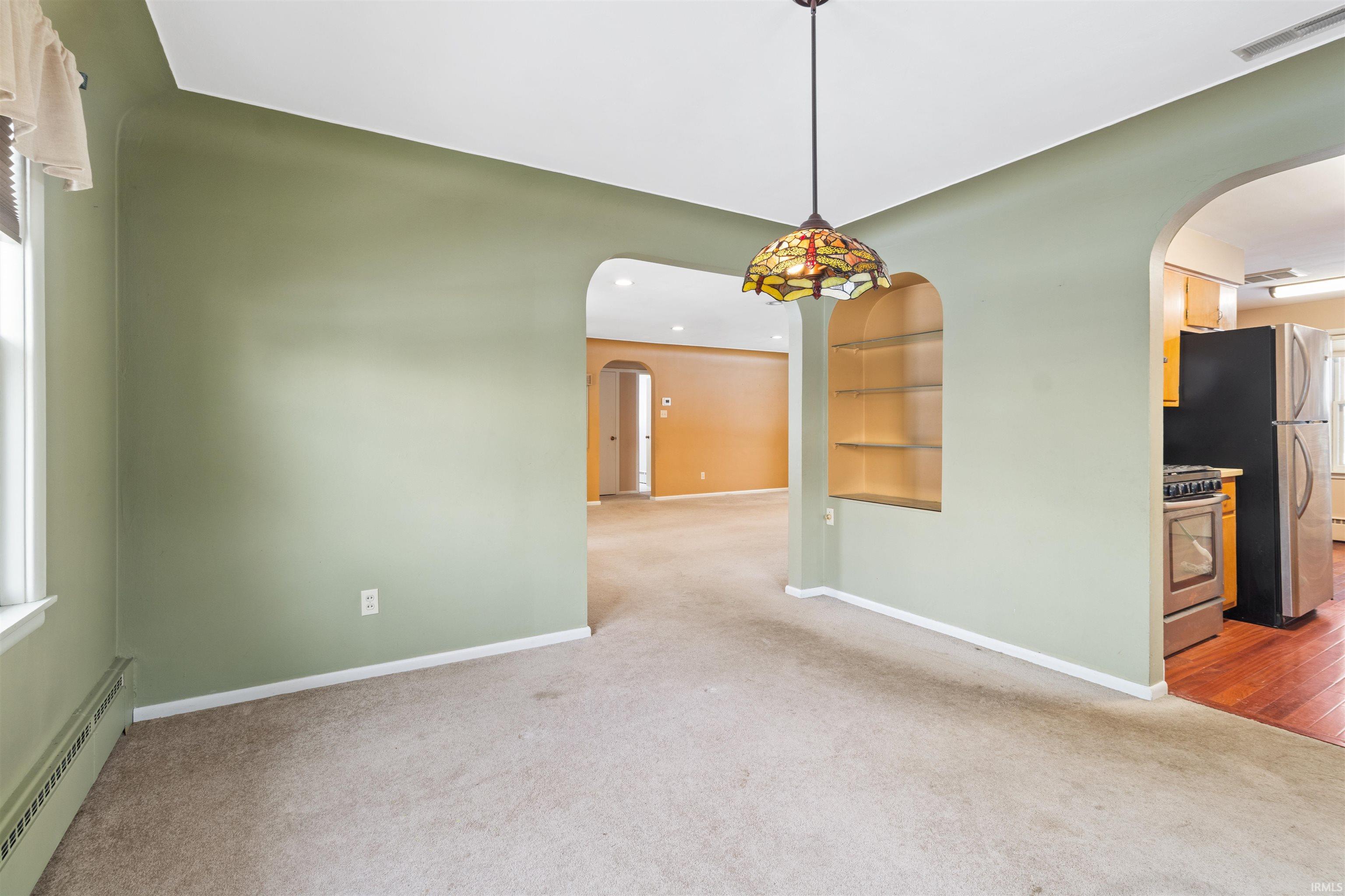 Unfurnished room with baseboard heating, arched walkways, light carpet, and built in features