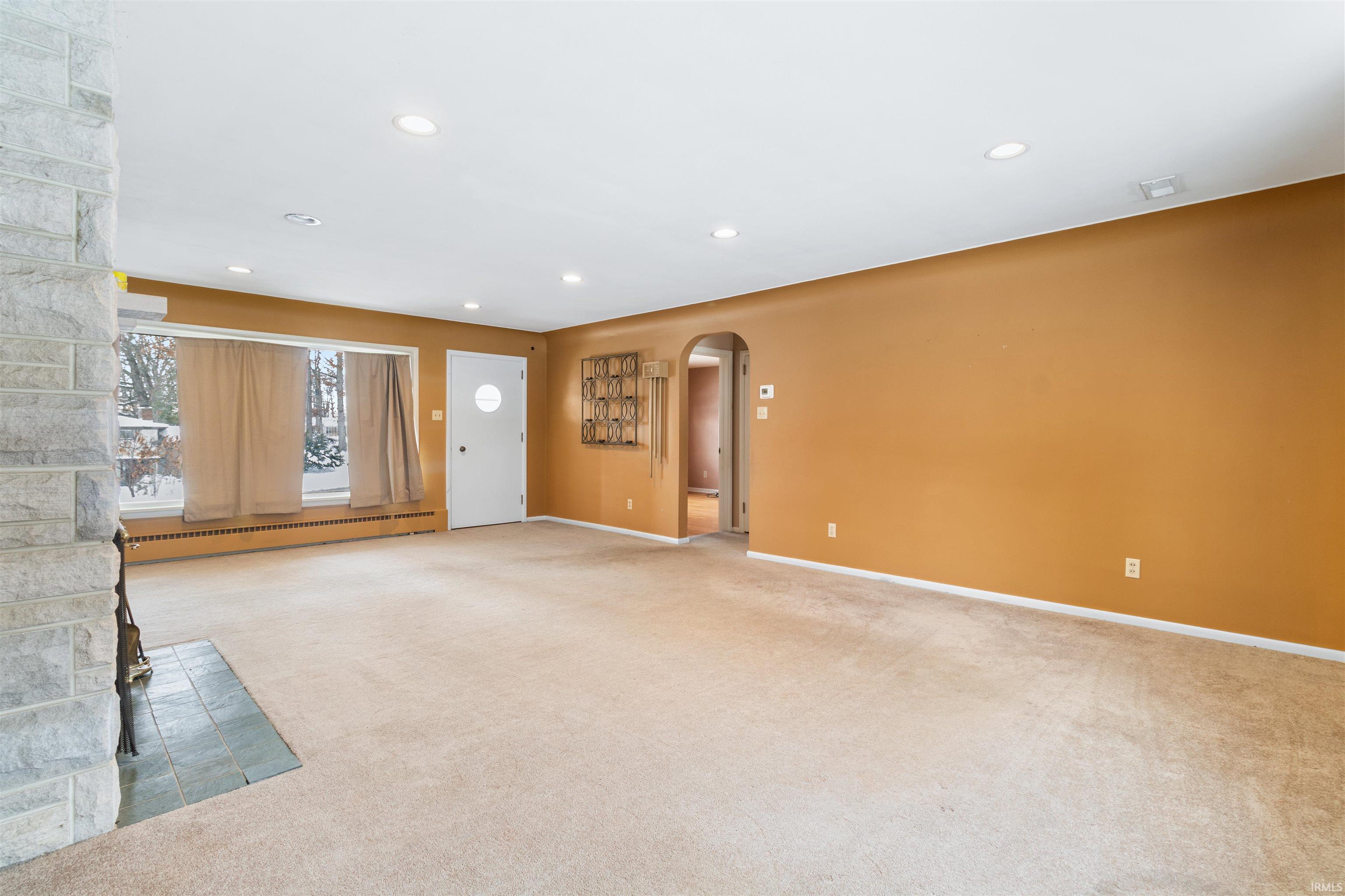 Unfurnished living room with arched walkways, light colored carpet, recessed lighting, and a baseboard heating unit