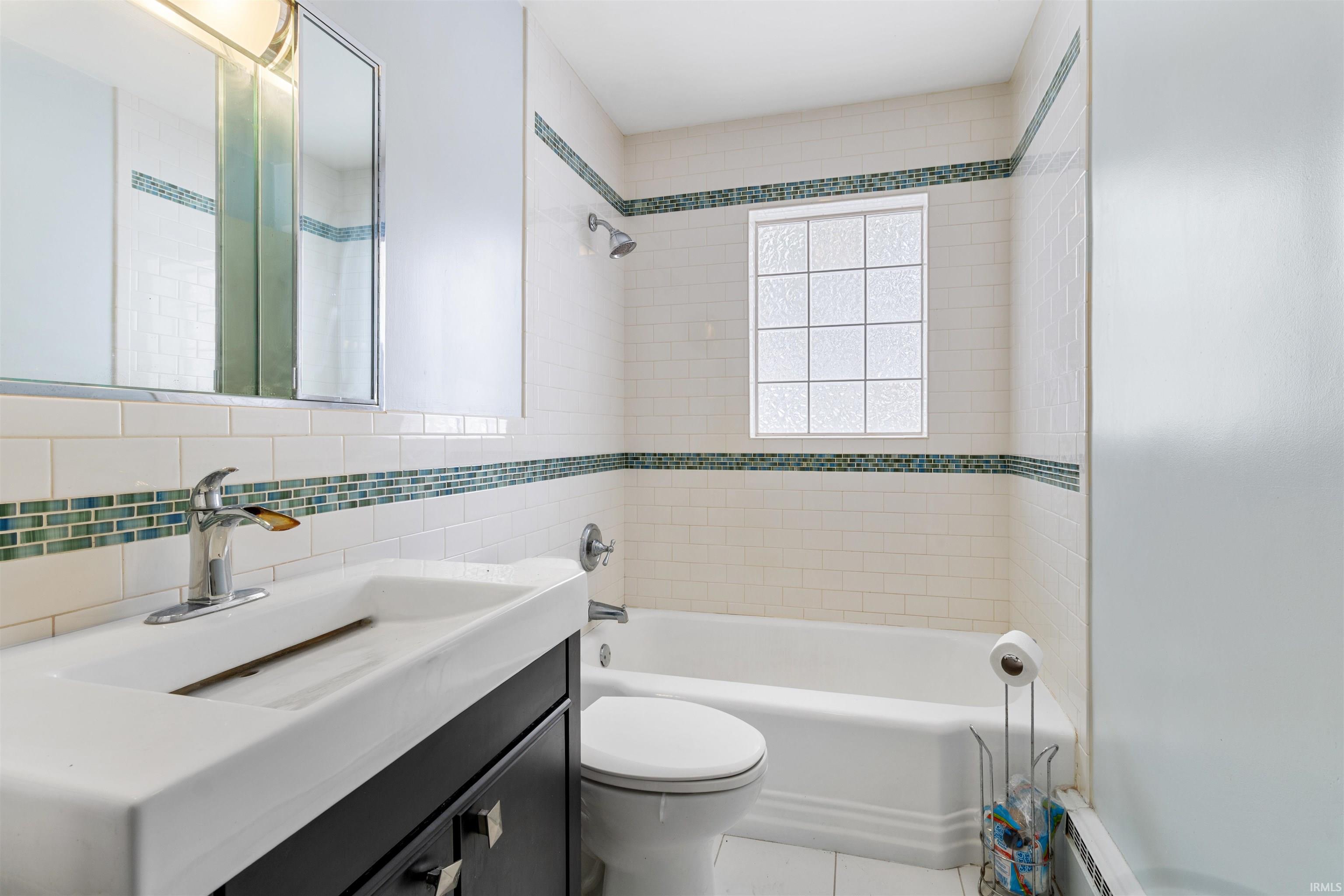 Bathroom with vanity, tile walls, shower / washtub combination, a baseboard heating unit, and tile patterned floors