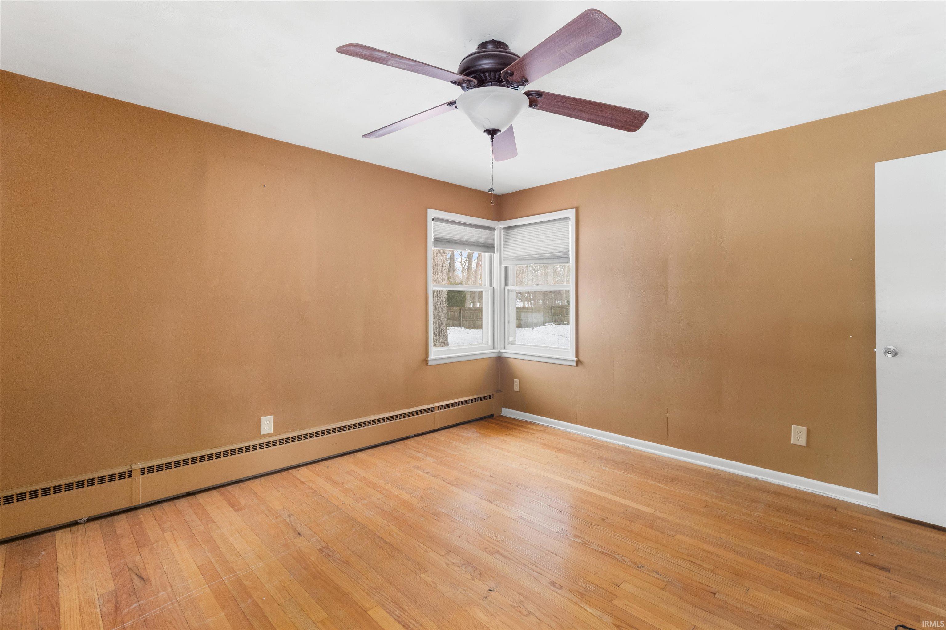 Unfurnished room with baseboard heating, hardwood / wood-style flooring, and a ceiling fan