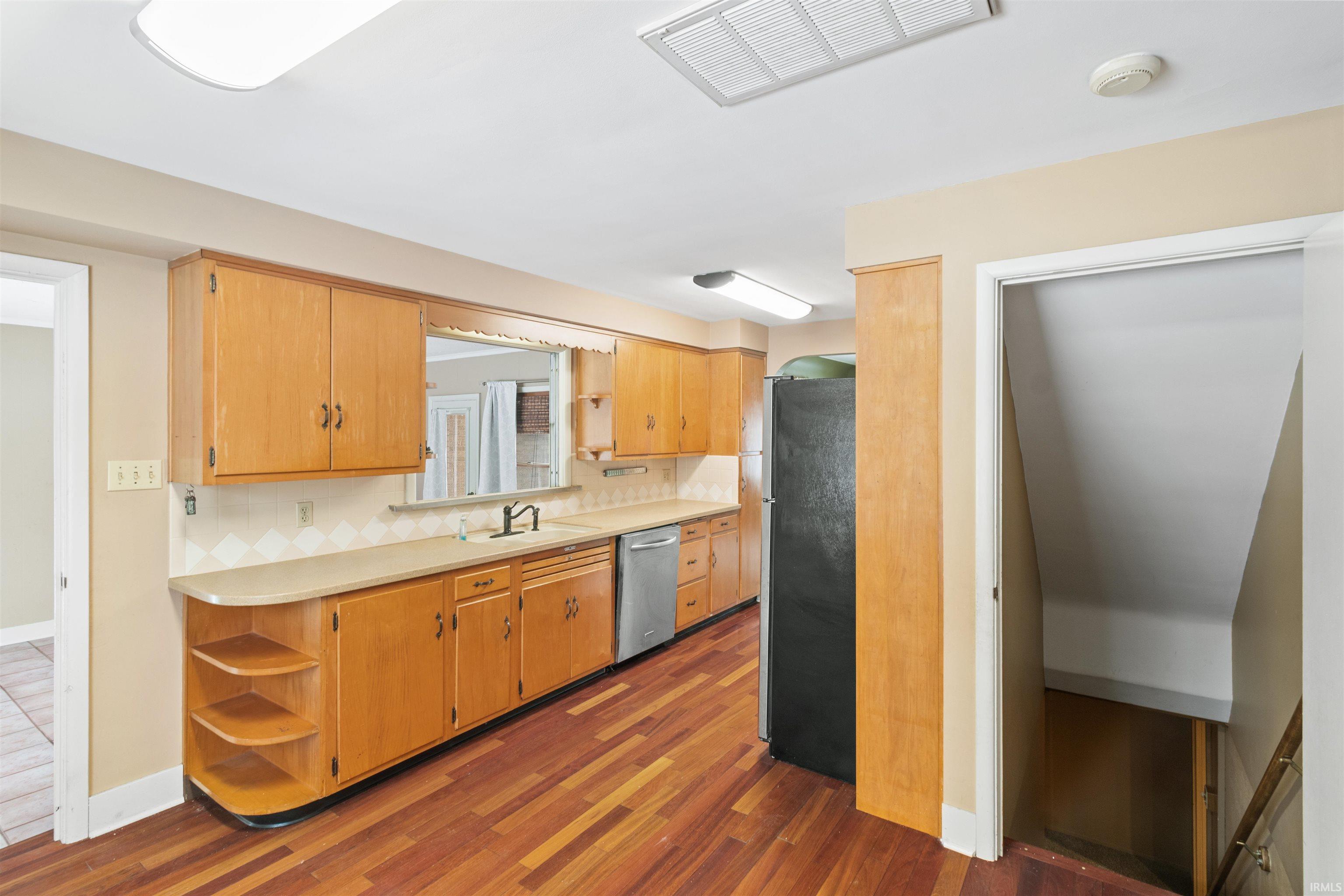Kitchen with light countertops, appliances with stainless steel finishes, open shelves, dark wood-style flooring, and tasteful backsplash