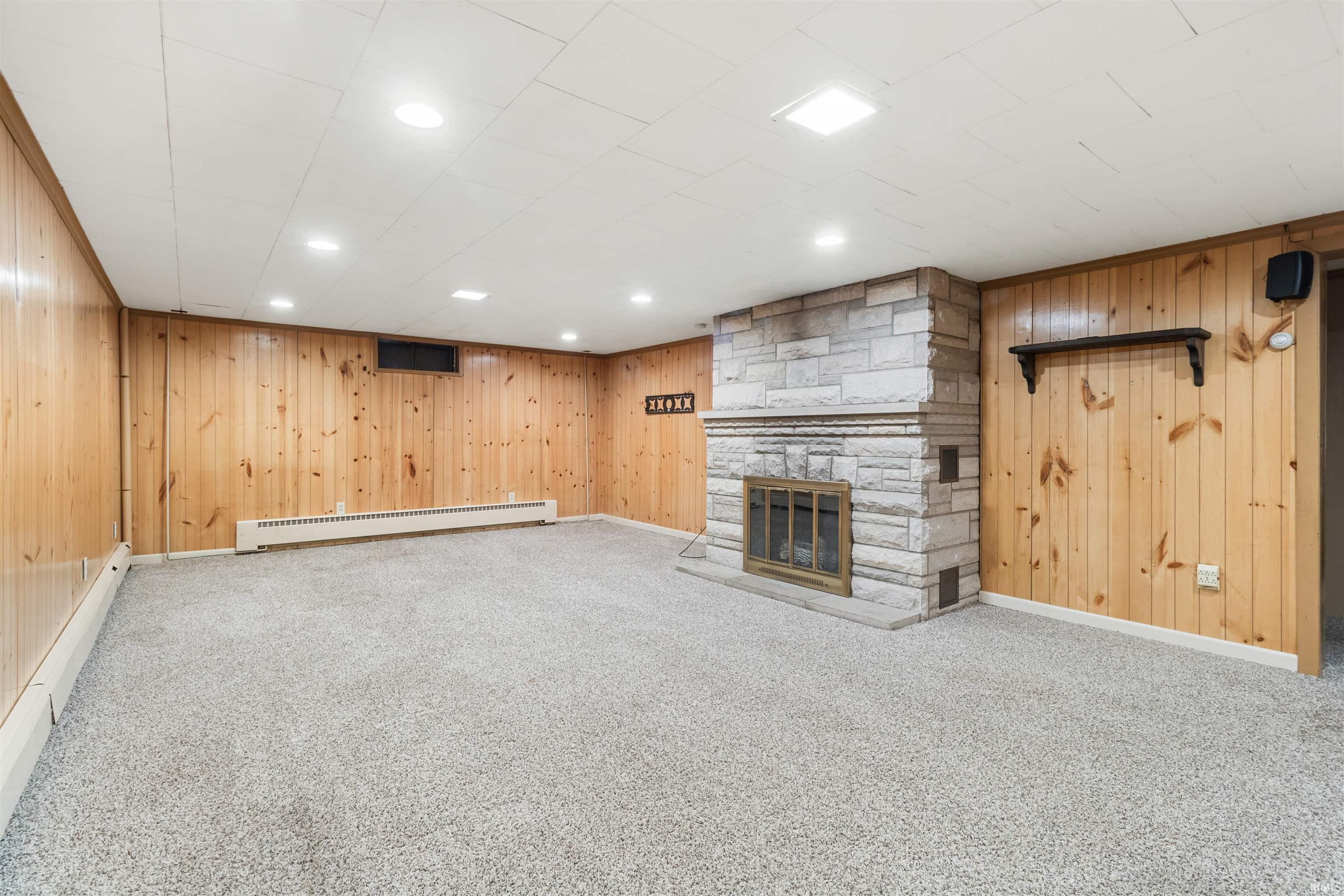 Unfurnished living room featuring wooden walls, a stone fireplace, carpet, baseboard heating, and recessed lighting