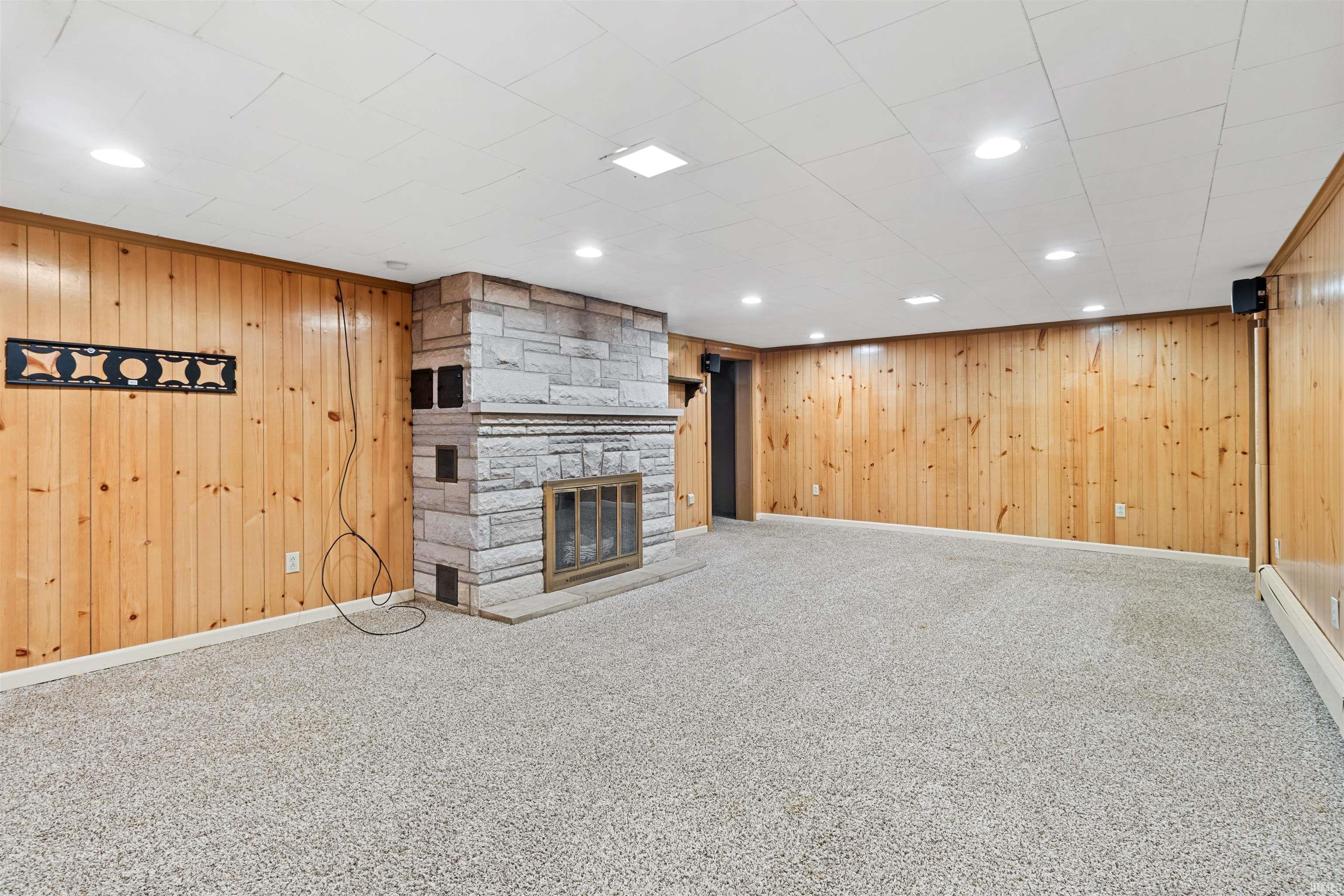 Unfurnished living room featuring a fireplace, carpet, wooden walls, recessed lighting, and a baseboard radiator