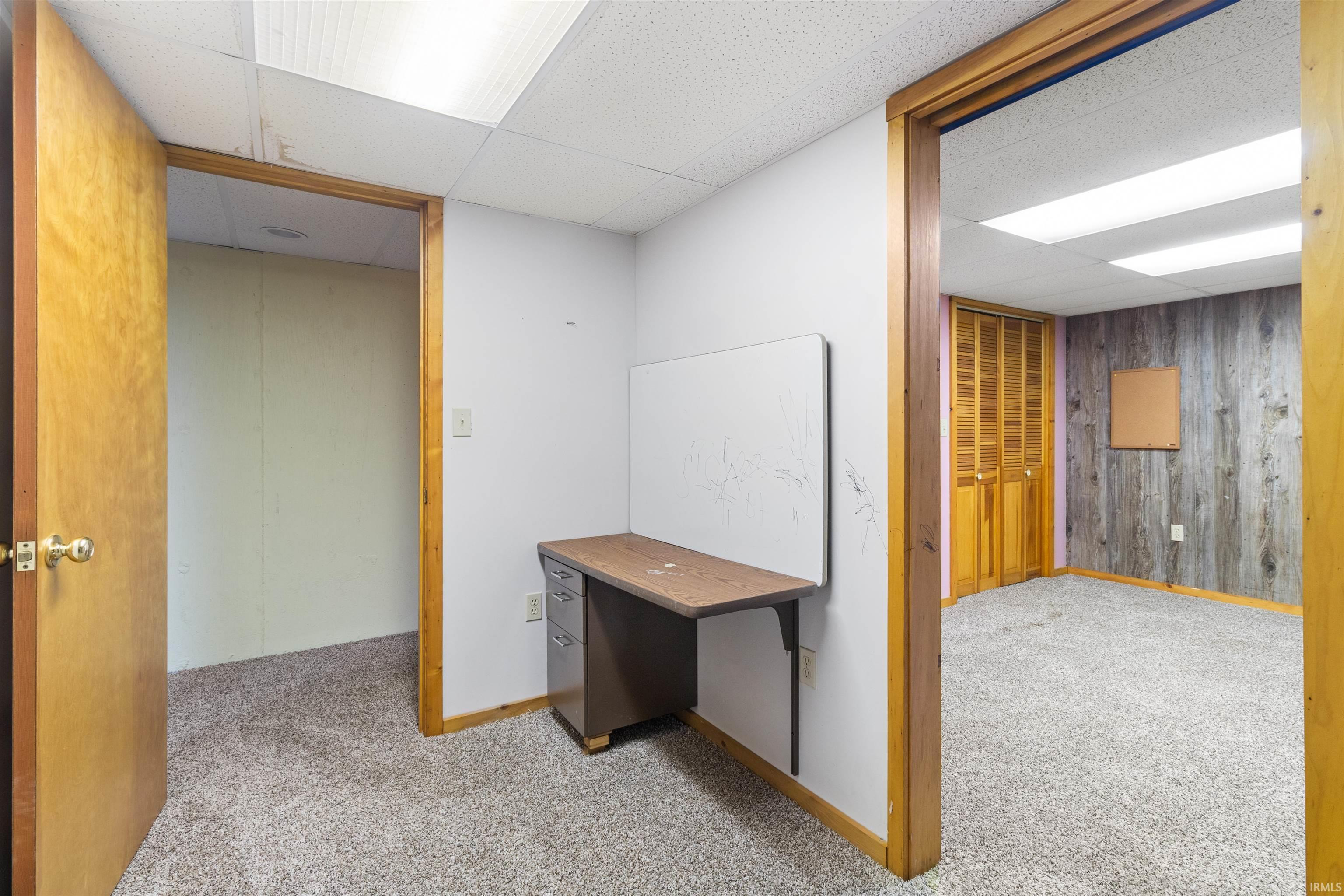 Hallway featuring carpet flooring, wood walls, and a paneled ceiling