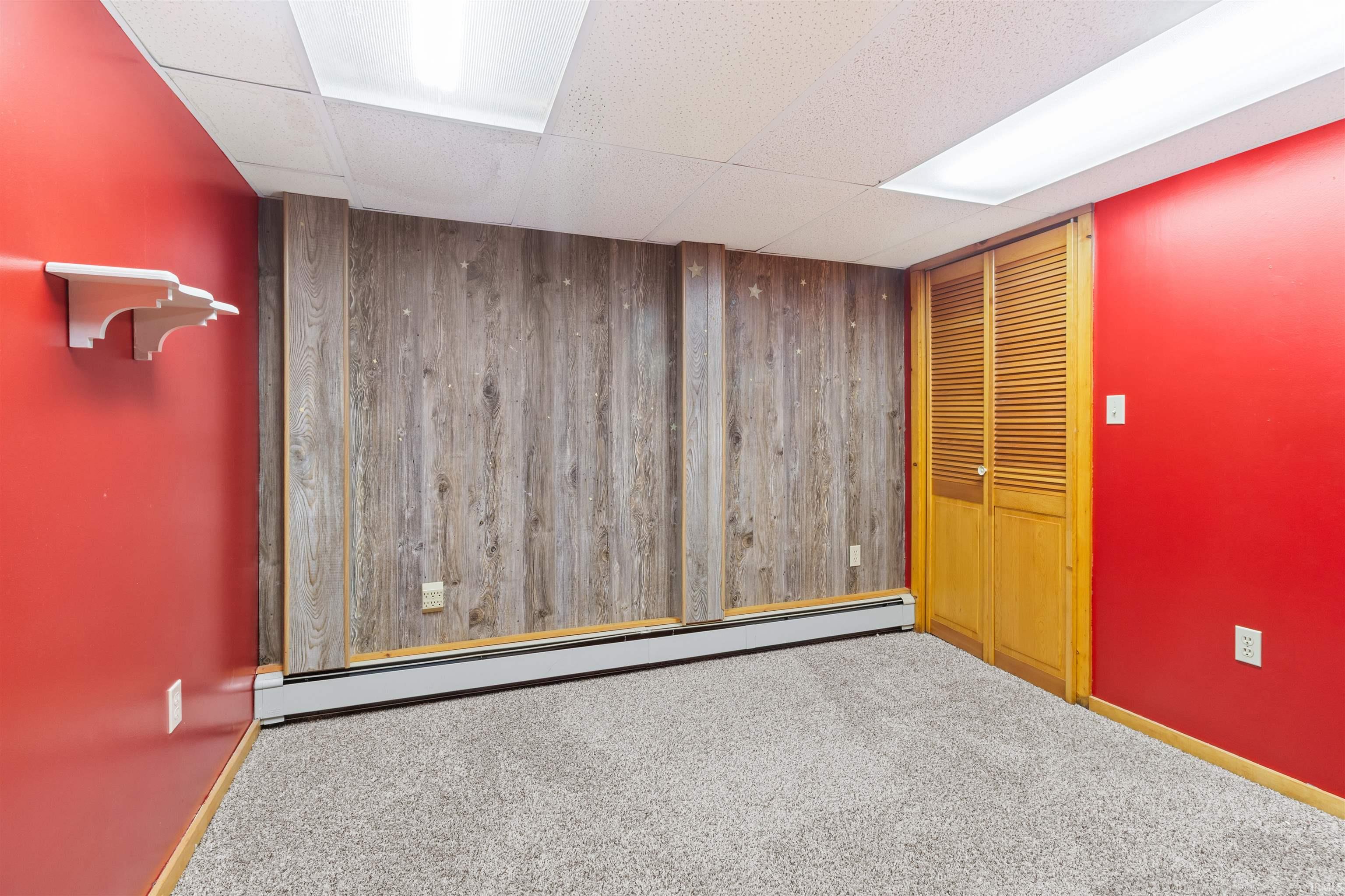 Carpeted spare room with a baseboard radiator, wooden walls, a drop ceiling, and an accent wall