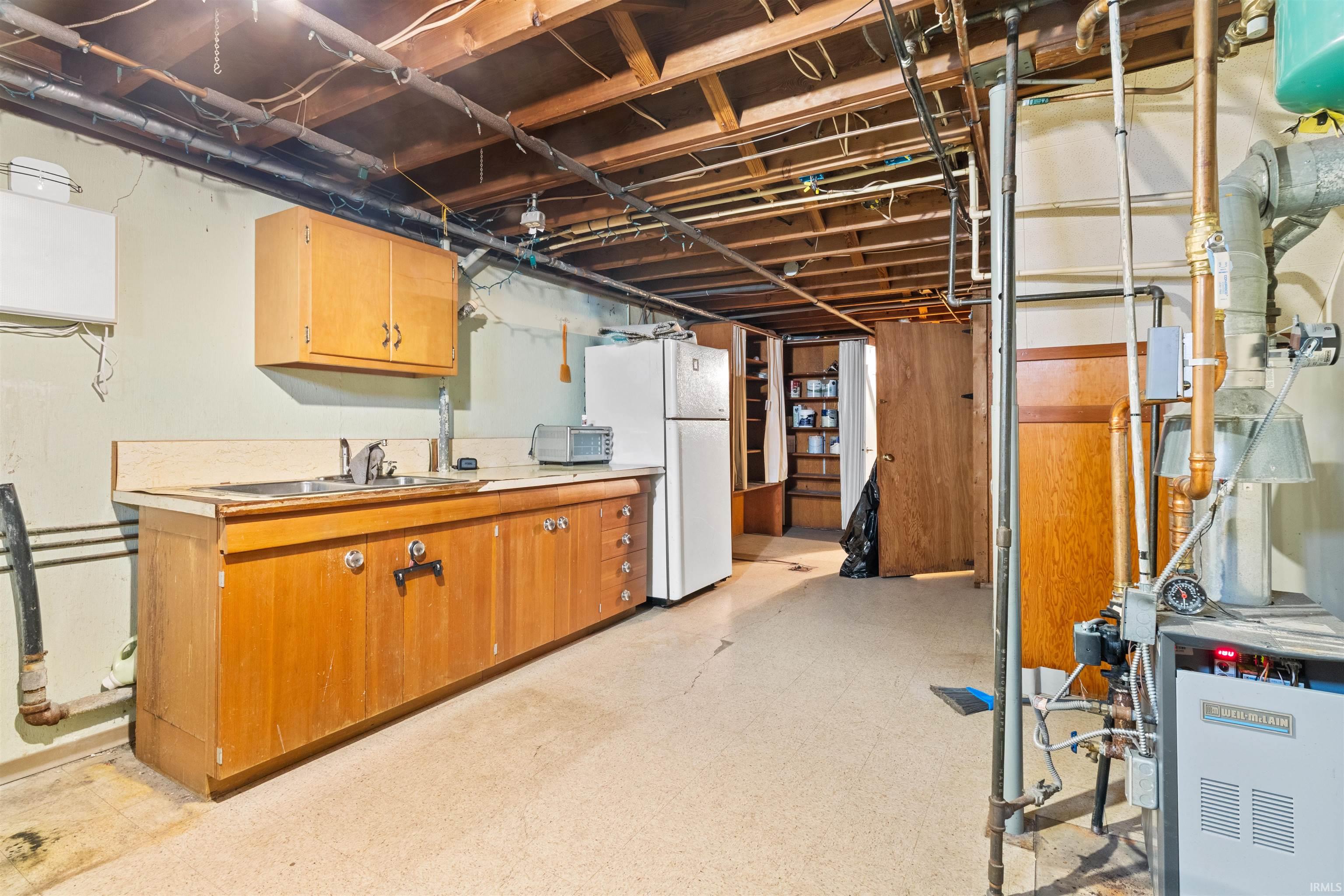 Unfinished below grade area with light floors and freestanding refrigerator