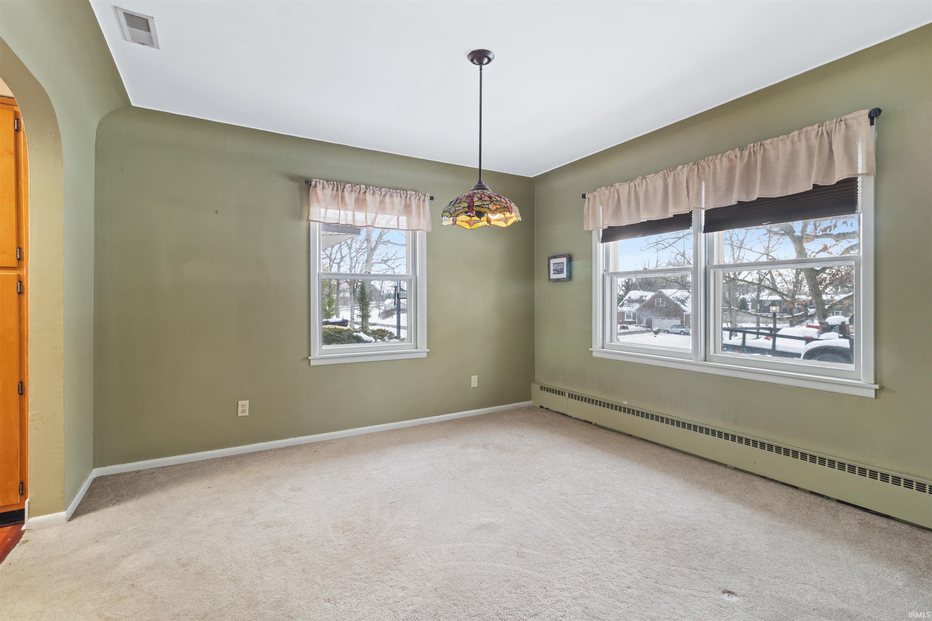 Carpeted spare room featuring arched walkways, plenty of natural light, and a baseboard radiator