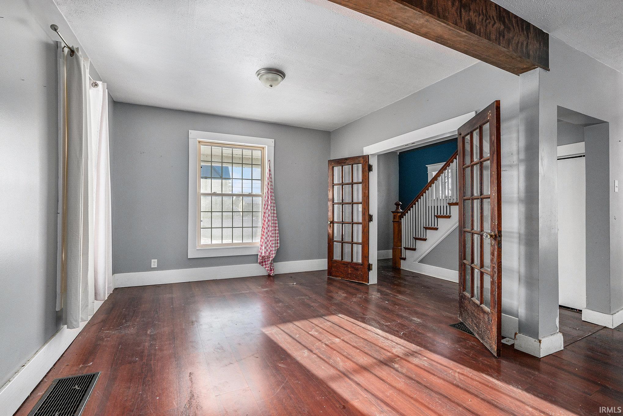 Unfurnished room featuring french doors, stairway, dark wood-type flooring, a textured ceiling, and beam ceiling