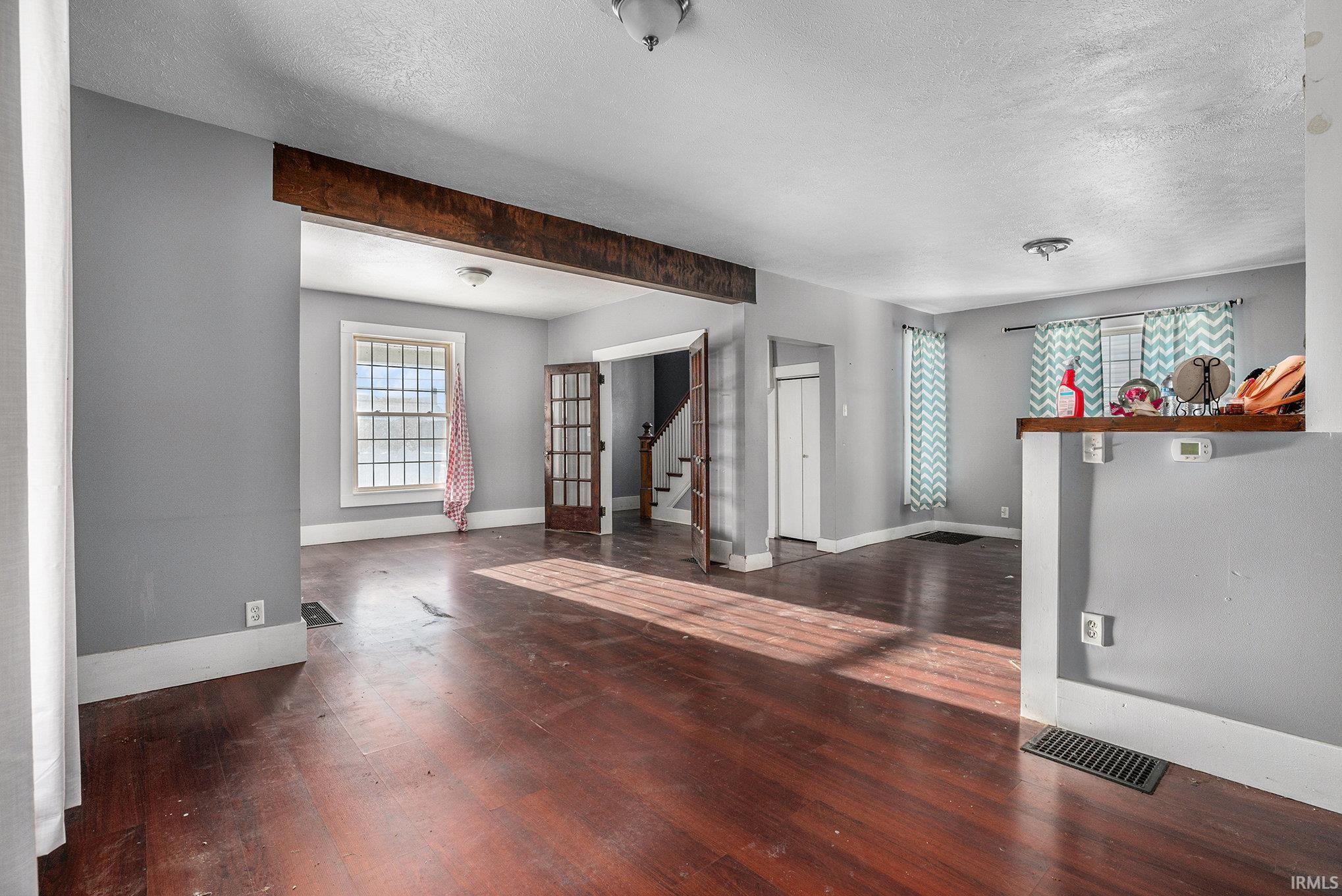 Unfurnished living room with dark wood-type flooring, a textured ceiling, stairs, and beam ceiling
