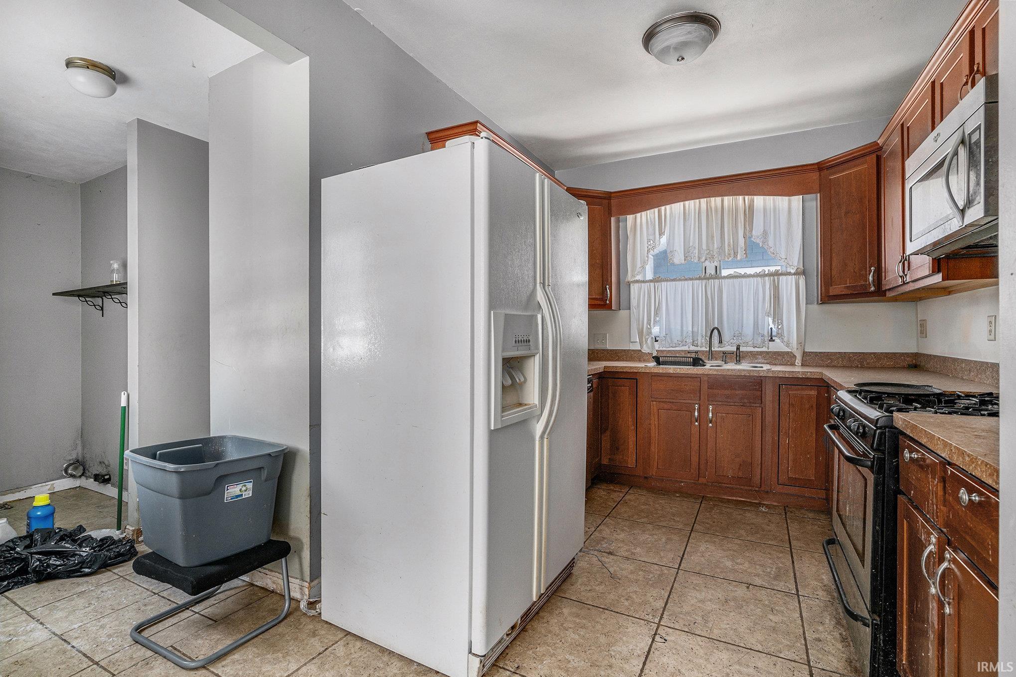 Kitchen with stainless steel appliances, brown cabinetry, light countertops, and light tile patterned floors