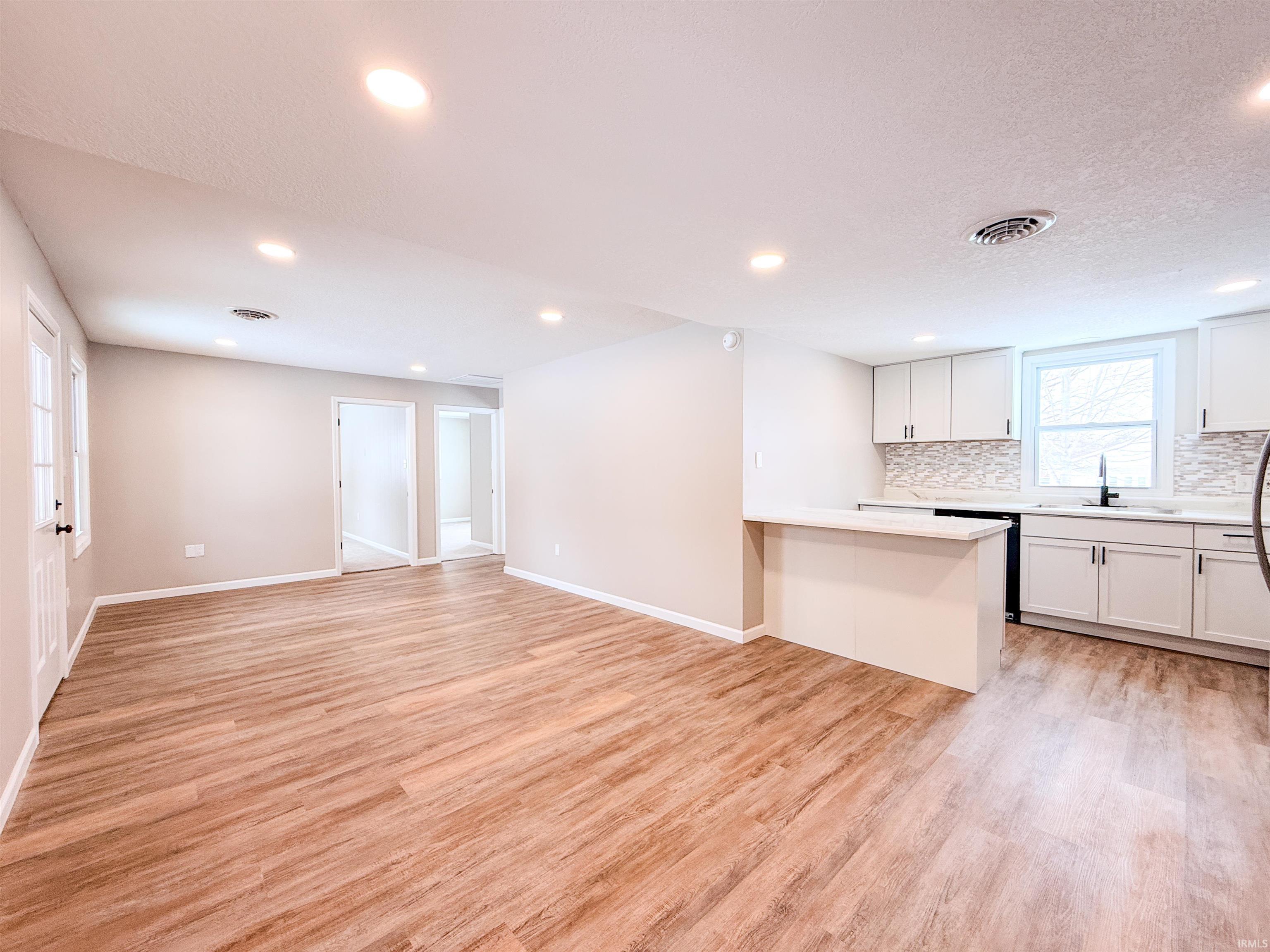 Kitchen with white cabinets, light wood-type flooring, a peninsula, open floor plan, and recessed lighting