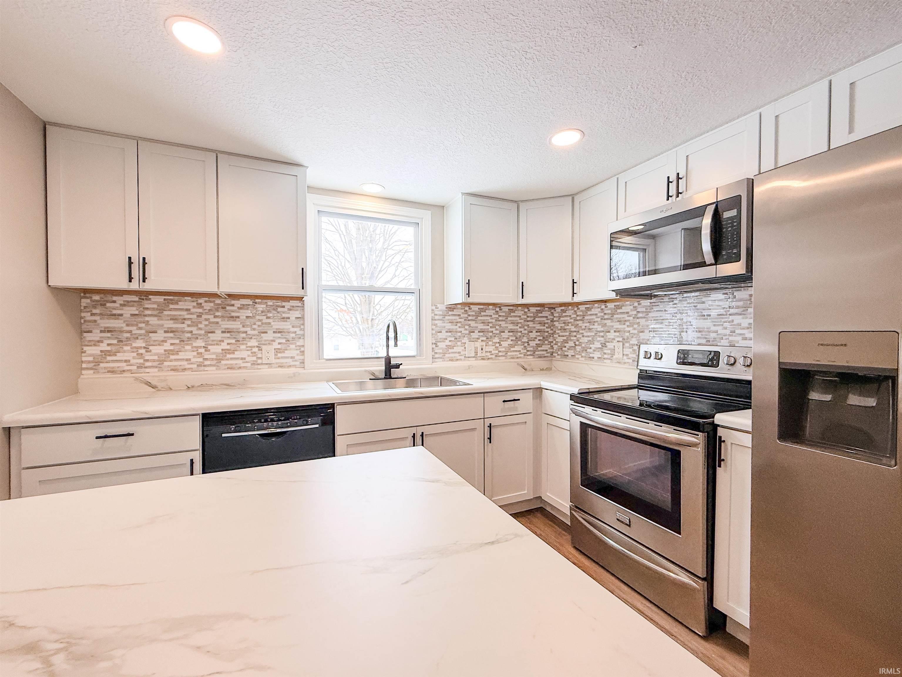 Kitchen with appliances with stainless steel finishes, white cabinets, a textured ceiling, recessed lighting, and light stone countertops