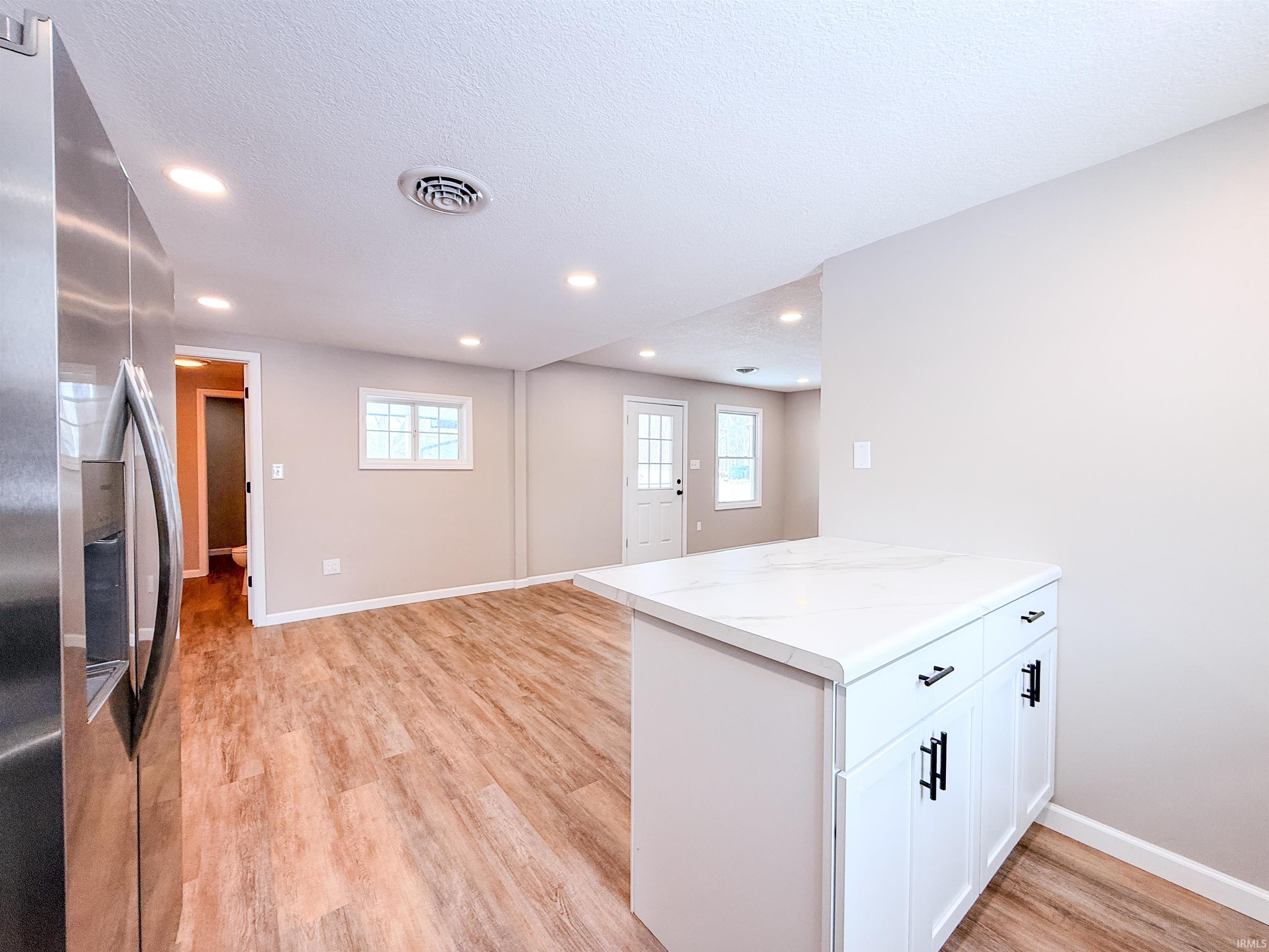 Kitchen featuring stainless steel fridge, white cabinetry, a peninsula, light countertops, and light wood-style floors