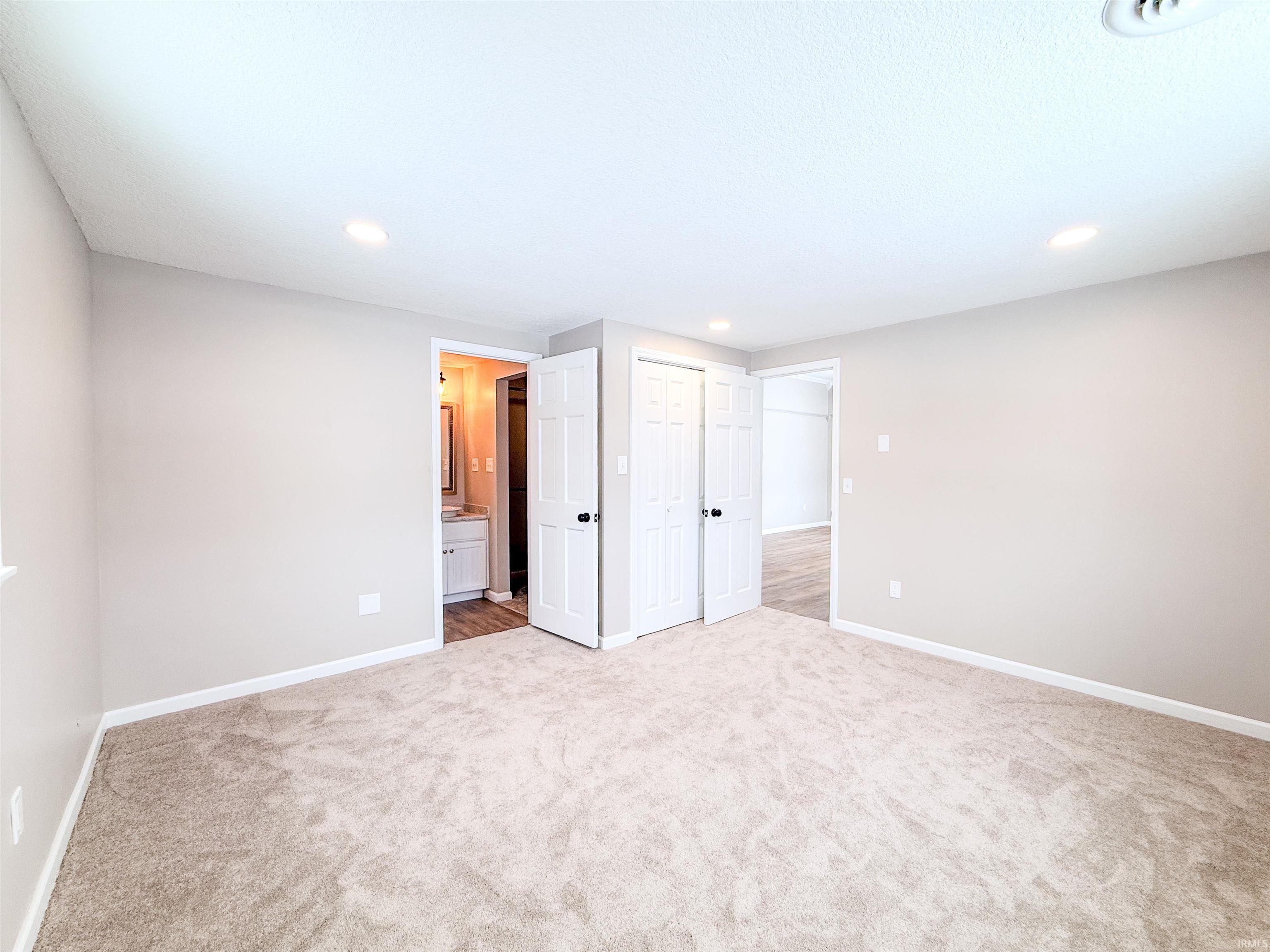 Unfurnished bedroom featuring ensuite bathroom, light colored carpet, a closet, and recessed lighting