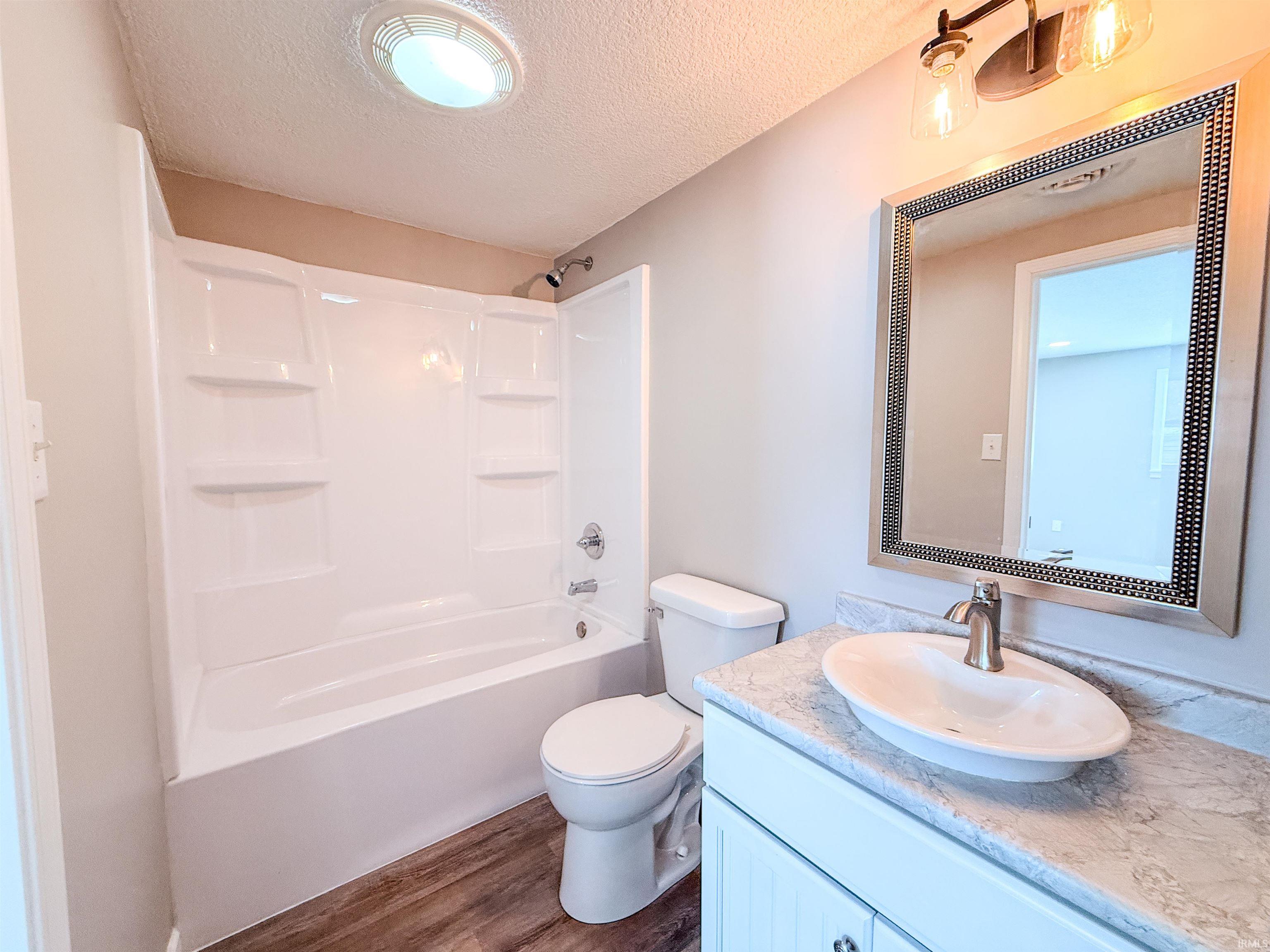 Full bath with vanity, a textured ceiling, washtub / shower combination, and dark wood finished floors