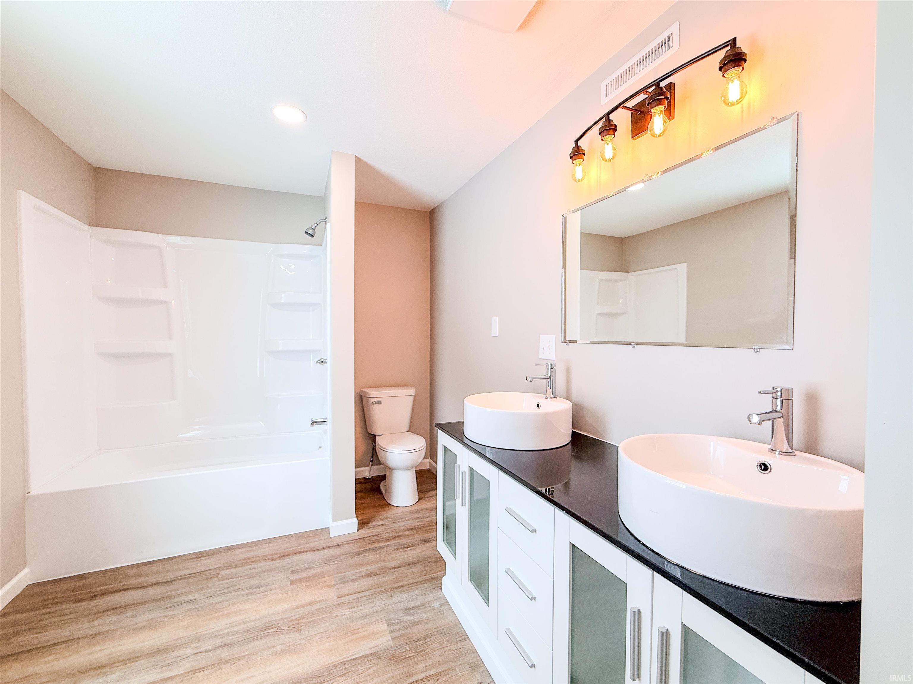 Full bathroom with double vanity, light wood-style flooring, tub / shower combination, and recessed lighting
