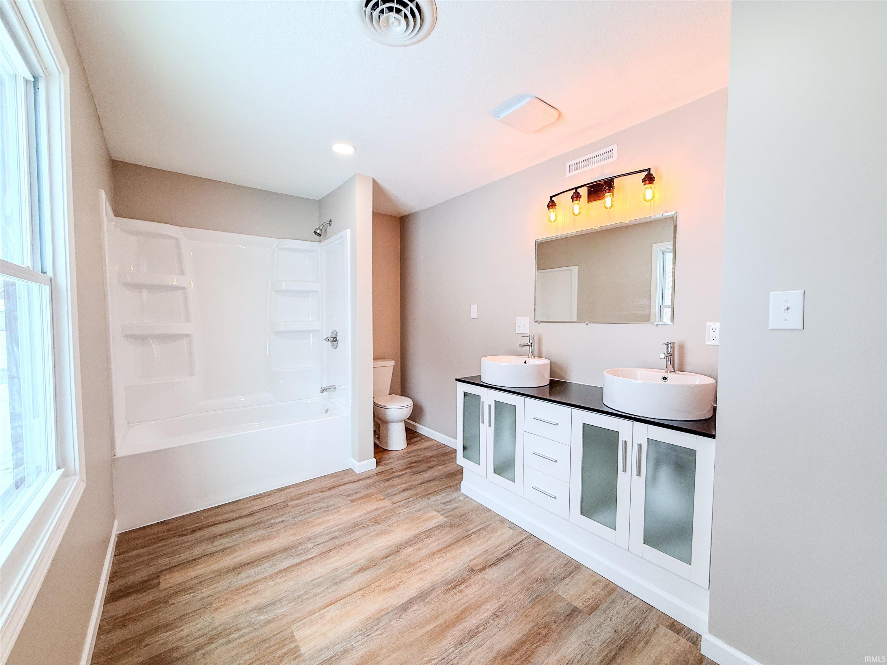 Bathroom with double vanity, tub / shower combination, light wood-style flooring, and recessed lighting