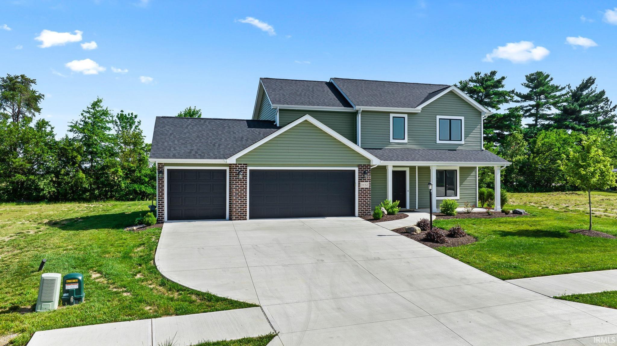 Two-story residence featuring green siding, dark brick accents, and a dark shingle roof