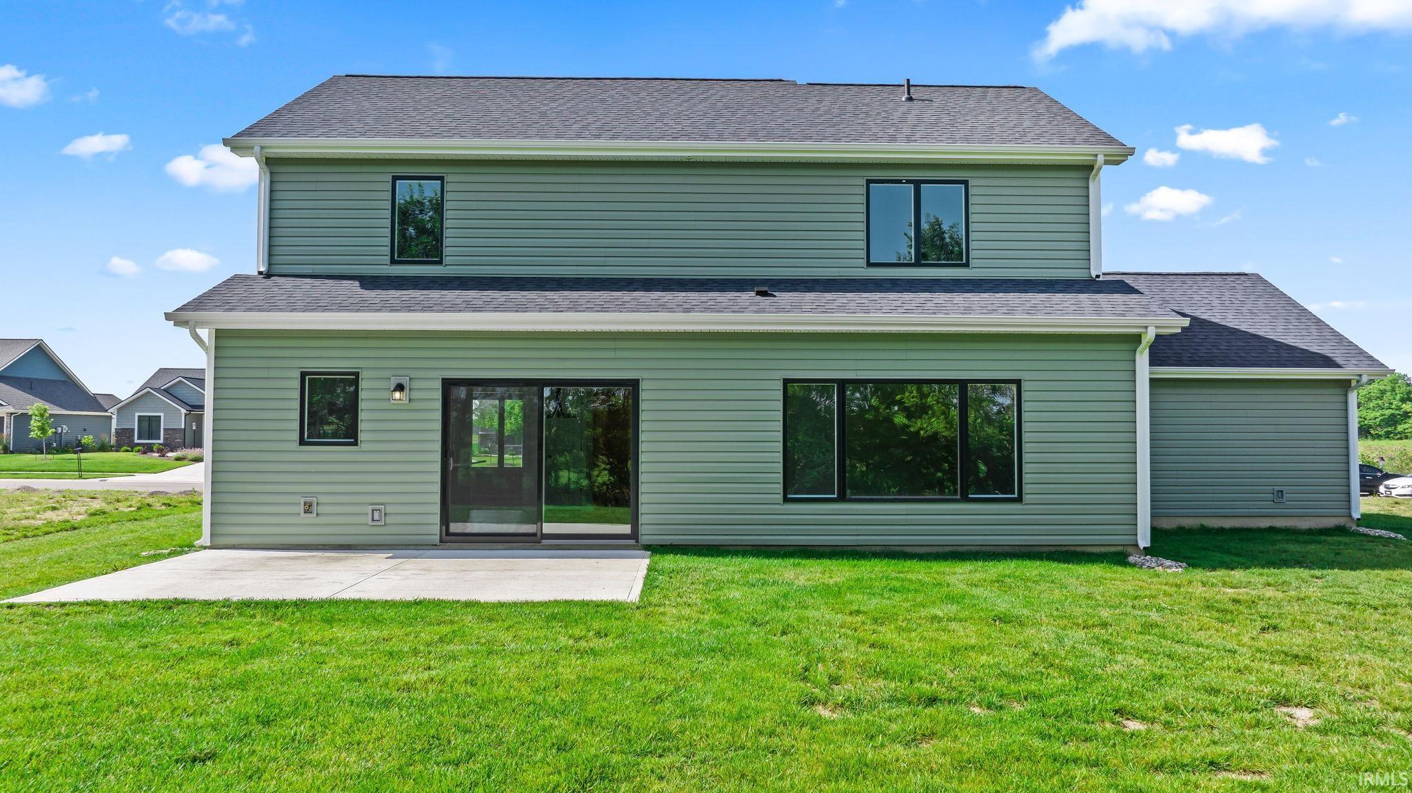 Rear exterior with green siding, a spacious concrete patio, large sliding glass doors, and multiple black-framed windows
