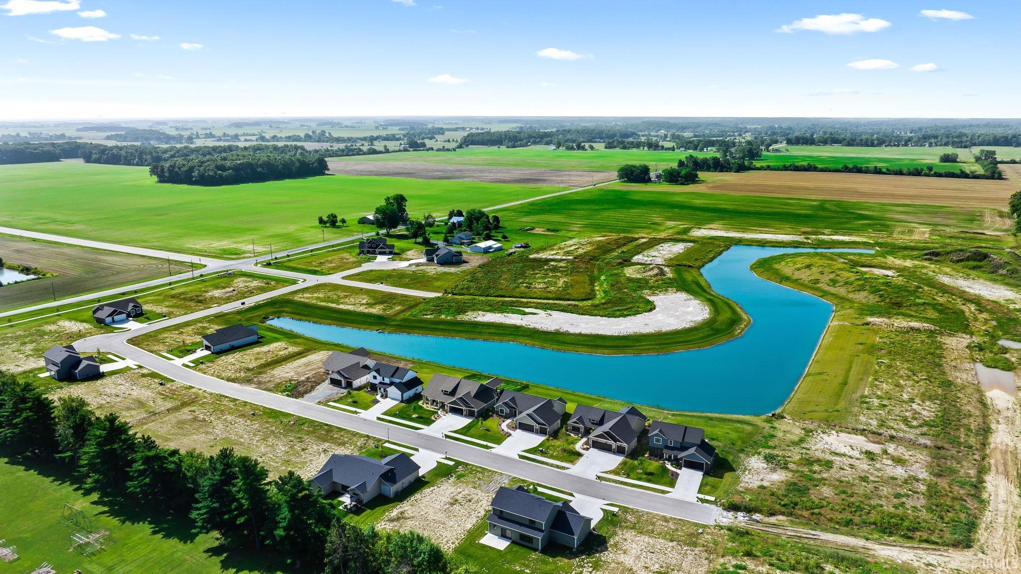 Expansive residential development featuring a large blue pond, paved streets, and new single-family homes