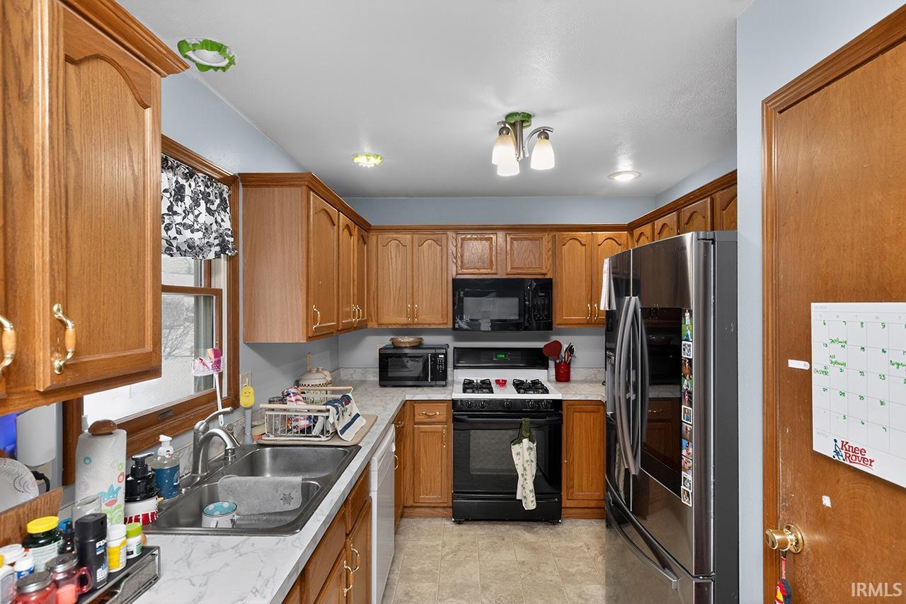 Kitchen with stainless steel fridge, gas range oven, brown cabinets, and black microwave