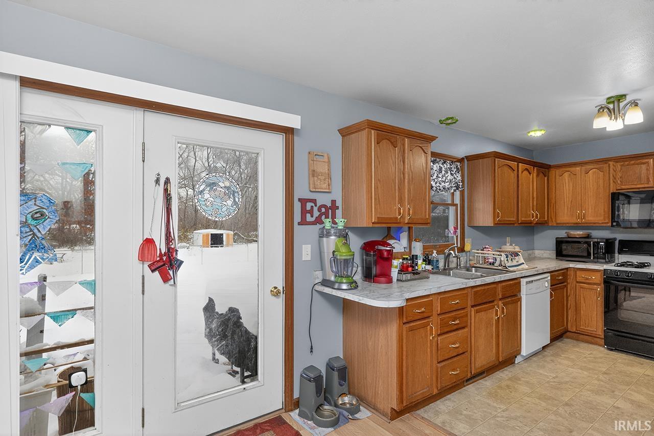 Kitchen with brown cabinetry, black appliances, and light countertops